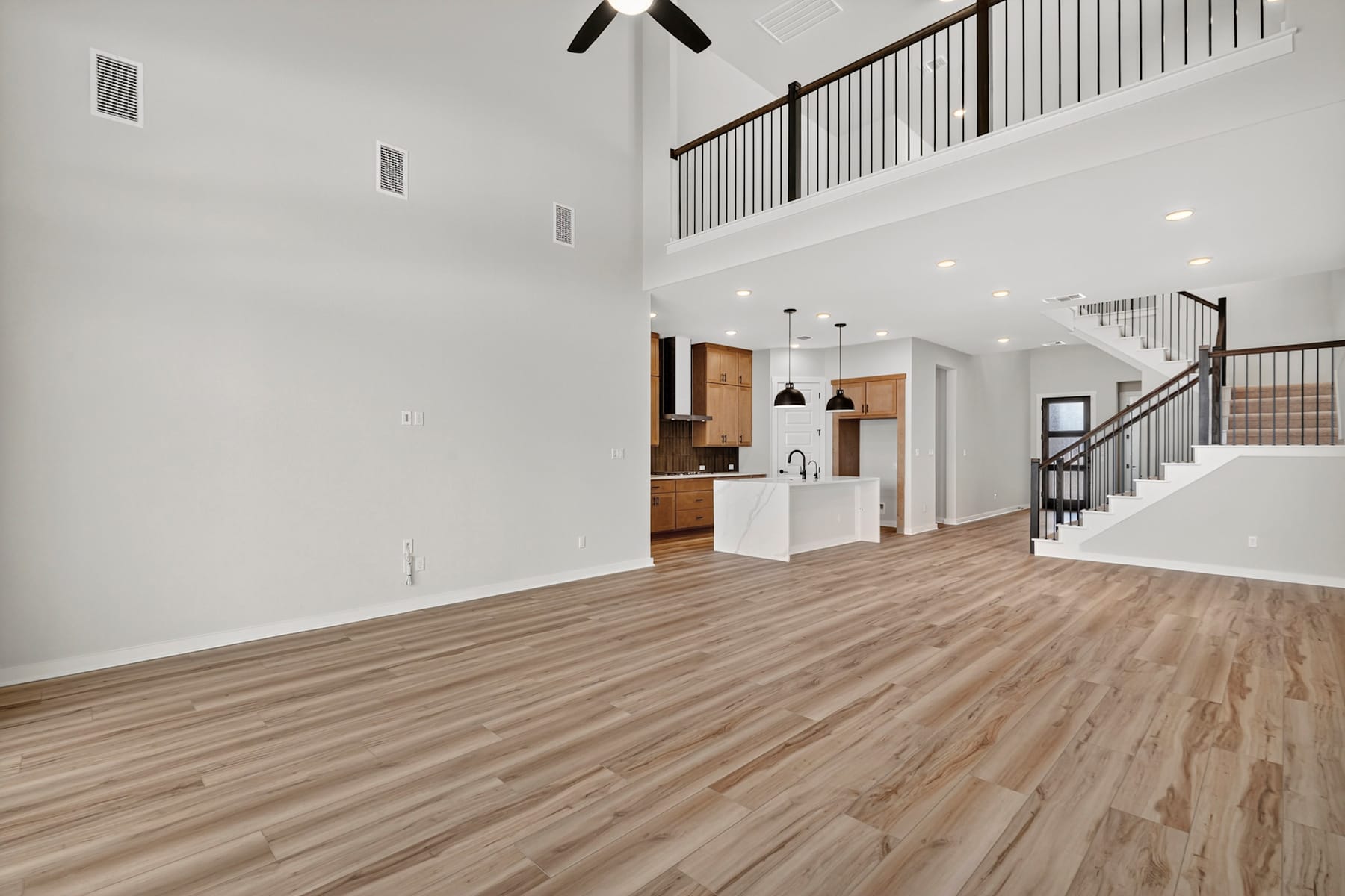 A spacious and modern interior with hardwood floors, a staircase, and a kitchen visible in the background.