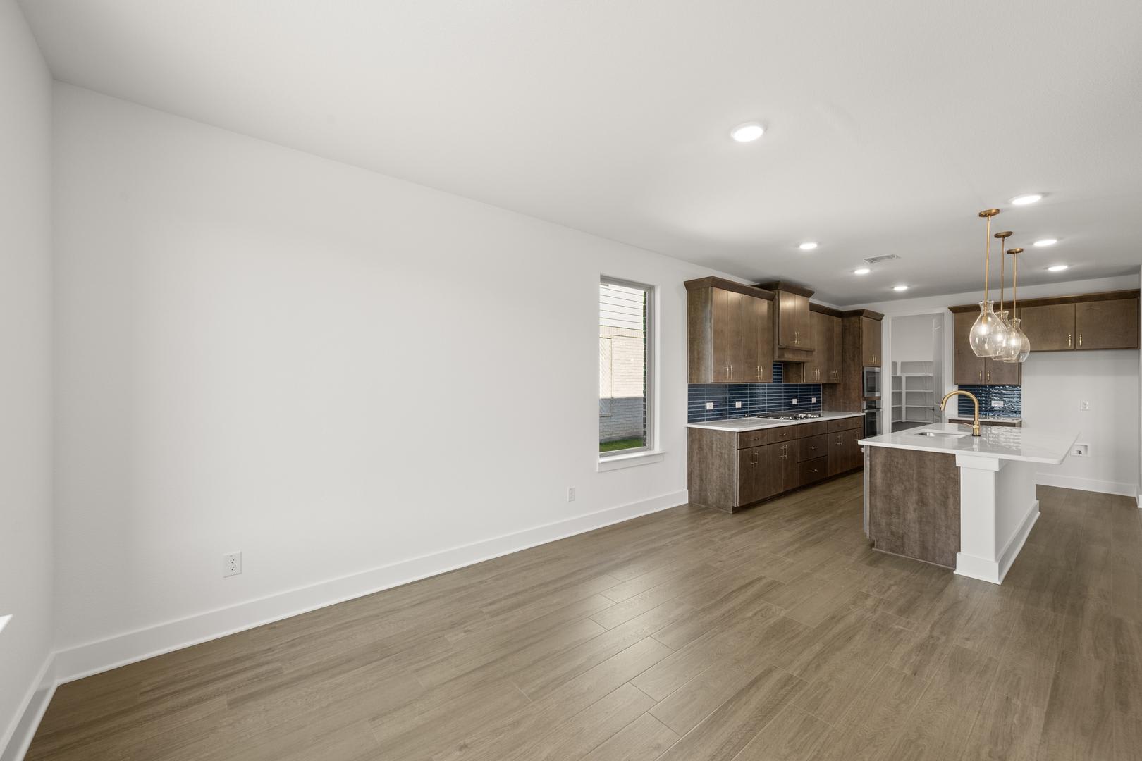A modern, open-concept kitchen and living space with white walls, dark wood cabinetry, and a hardwood floor.