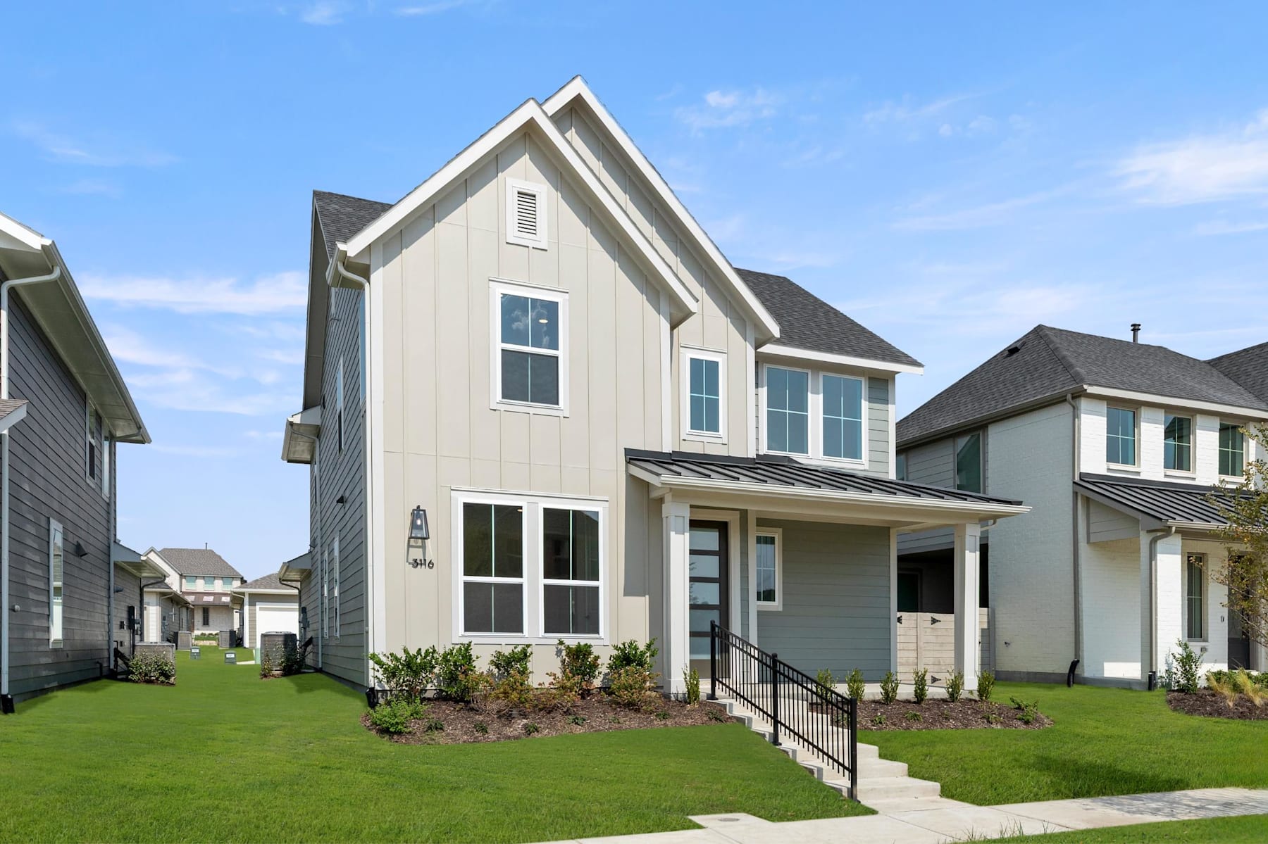 A modern two-story house with a gabled roof, gray siding, and a well-manicured lawn in the foreground, set against a clear blue sky.