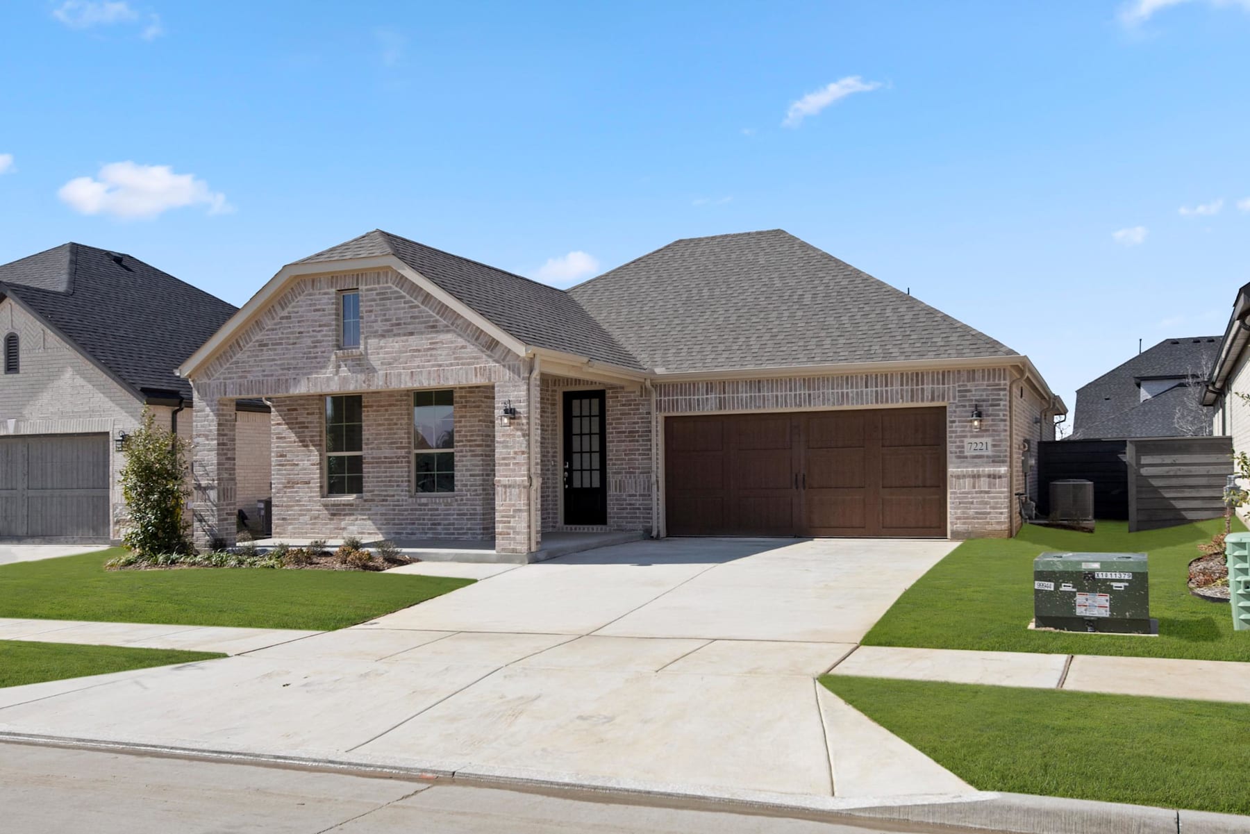 A two-story residential house with a garage, surrounded by a well-manicured lawn and a paved driveway, set against a clear blue sky with scattered clouds.