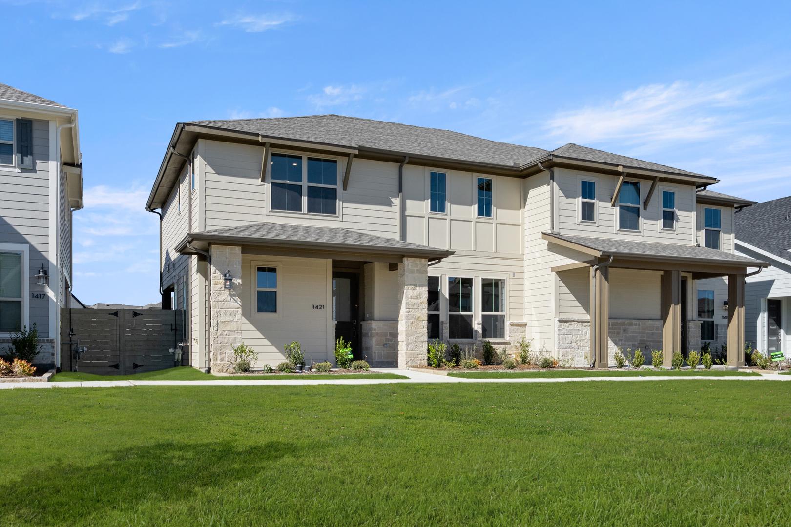 A well-manicured lawn in the foreground leads to a modern, two-story residential building with a mix of siding materials and large windows against a clear blue sky.