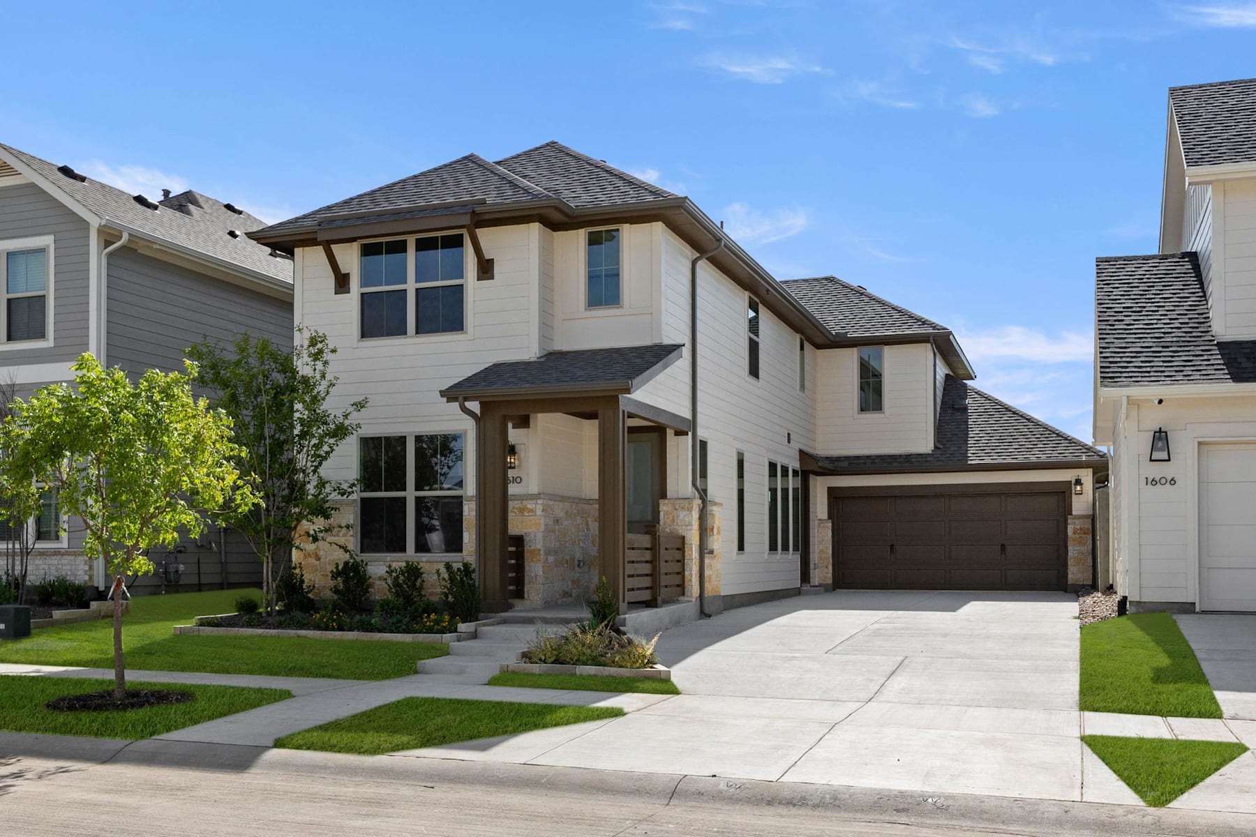 A two-story residential house with a garage, surrounded by a well-manicured lawn and landscaping, set against a clear blue sky with some clouds.