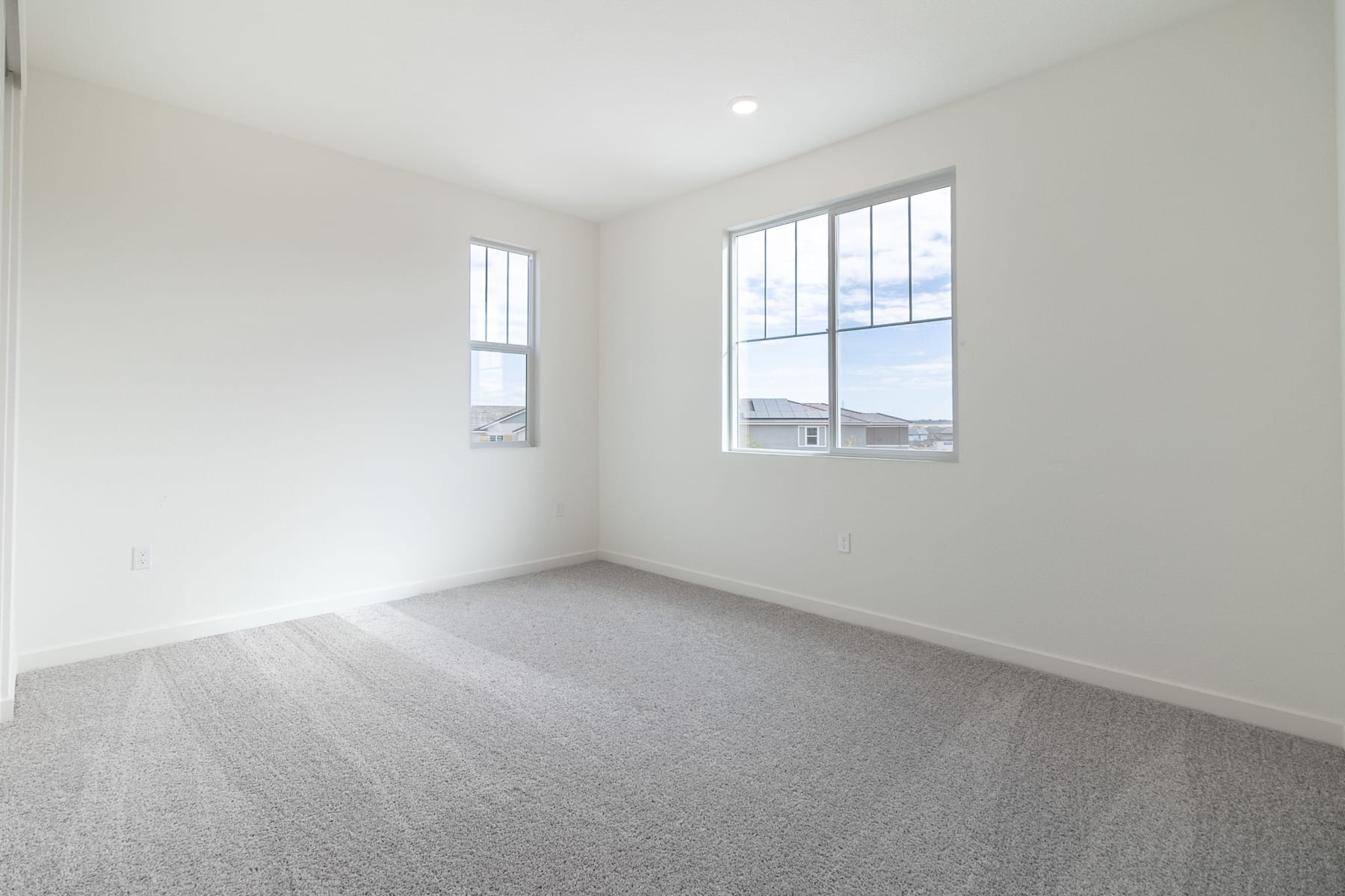 A spacious, well-lit room with large windows, a neutral-colored carpet, and a clean, minimalist aesthetic.