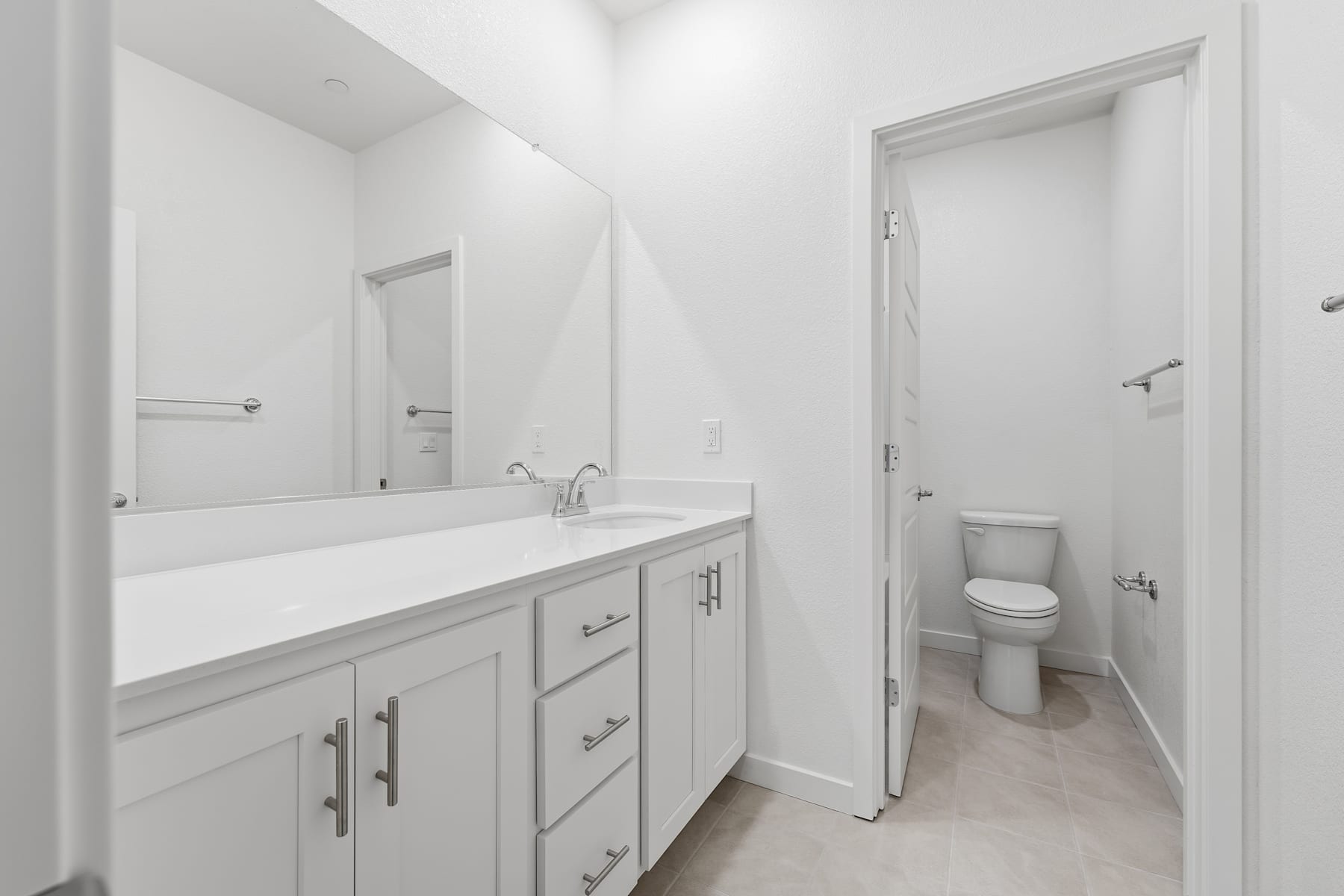 A modern, minimalist bathroom with a white vanity, mirror, and toilet visible in the background.