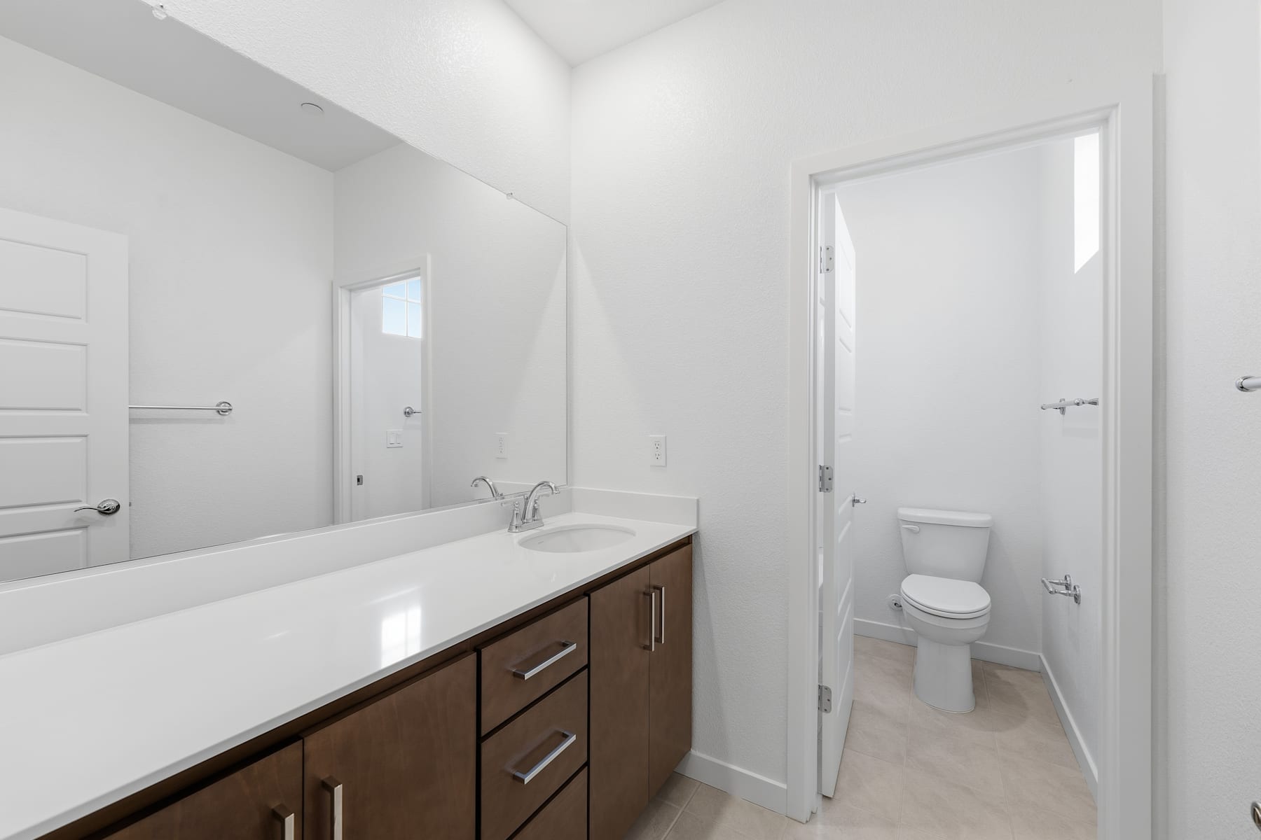A modern, minimalist bathroom with a white vanity, wooden cabinets, and a toilet visible in the background.