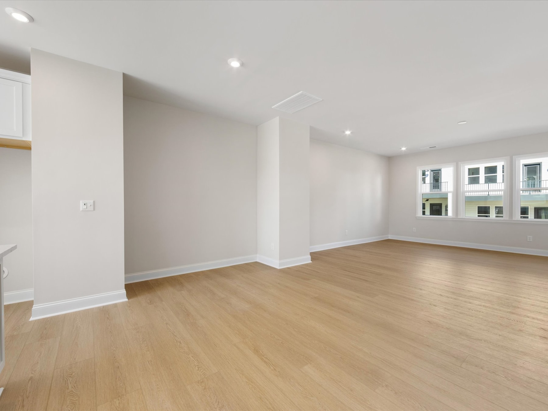 A spacious, well-lit room with white walls and a hardwood floor, featuring a window overlooking the exterior.