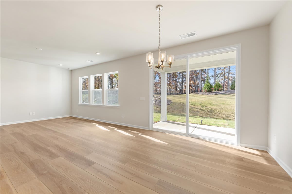 A spacious and bright room with hardwood floors, large windows overlooking a lush outdoor landscape, and a decorative chandelier hanging from the ceiling.