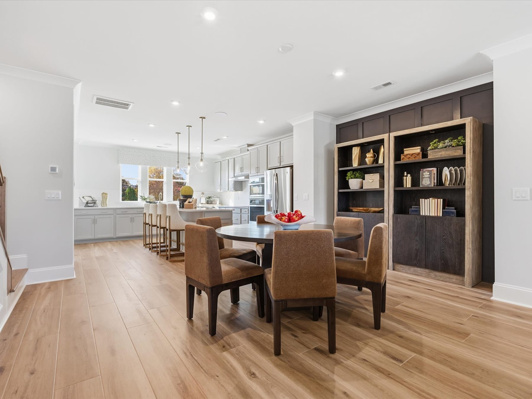 A modern and spacious open-plan kitchen and dining area with wooden floors, built-in shelving, and a dining table with chairs.