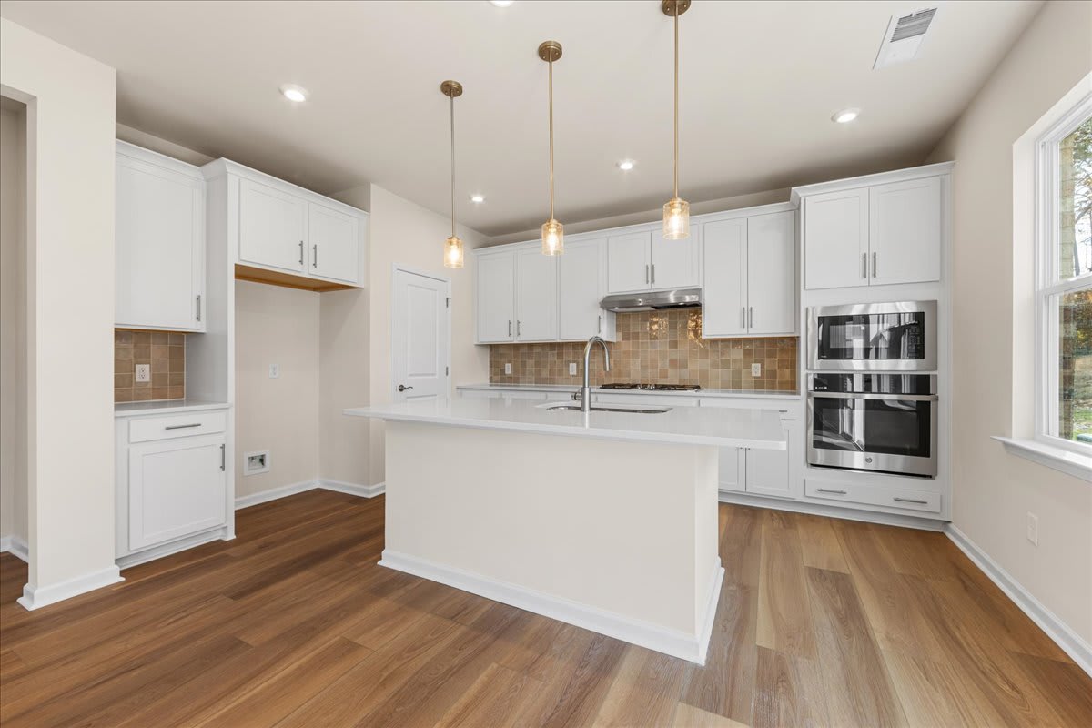 A modern, bright kitchen with white cabinets, wooden floors, and pendant lights hanging from the ceiling.