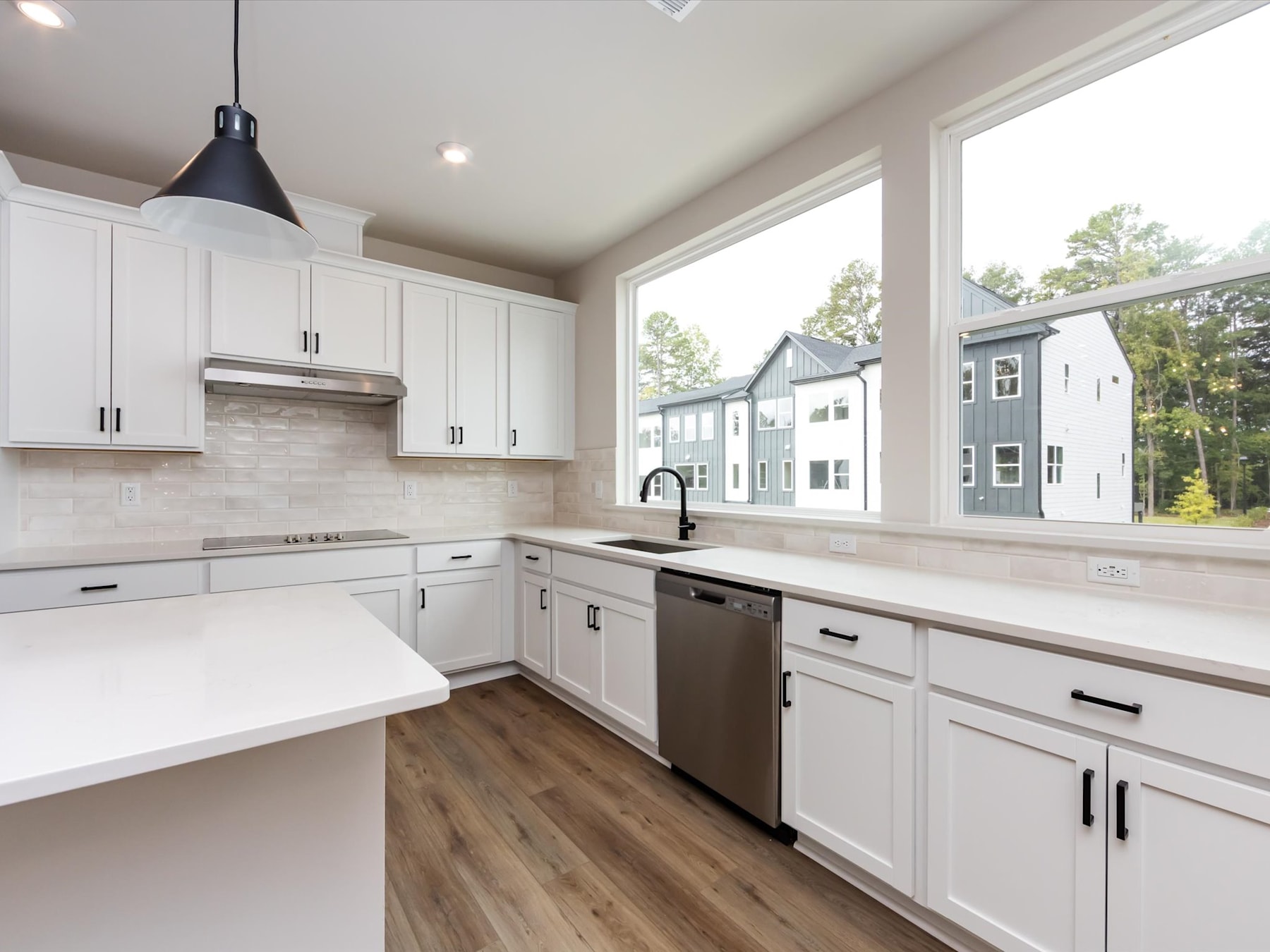 A modern, bright kitchen with white cabinets, stainless steel appliances, and a large window overlooking a residential neighborhood.