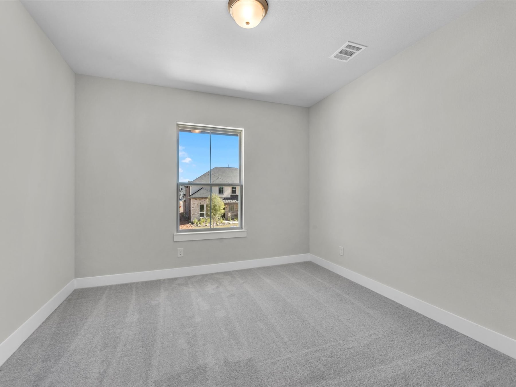 A sparsely furnished room with a single window overlooking a residential neighborhood in the background.