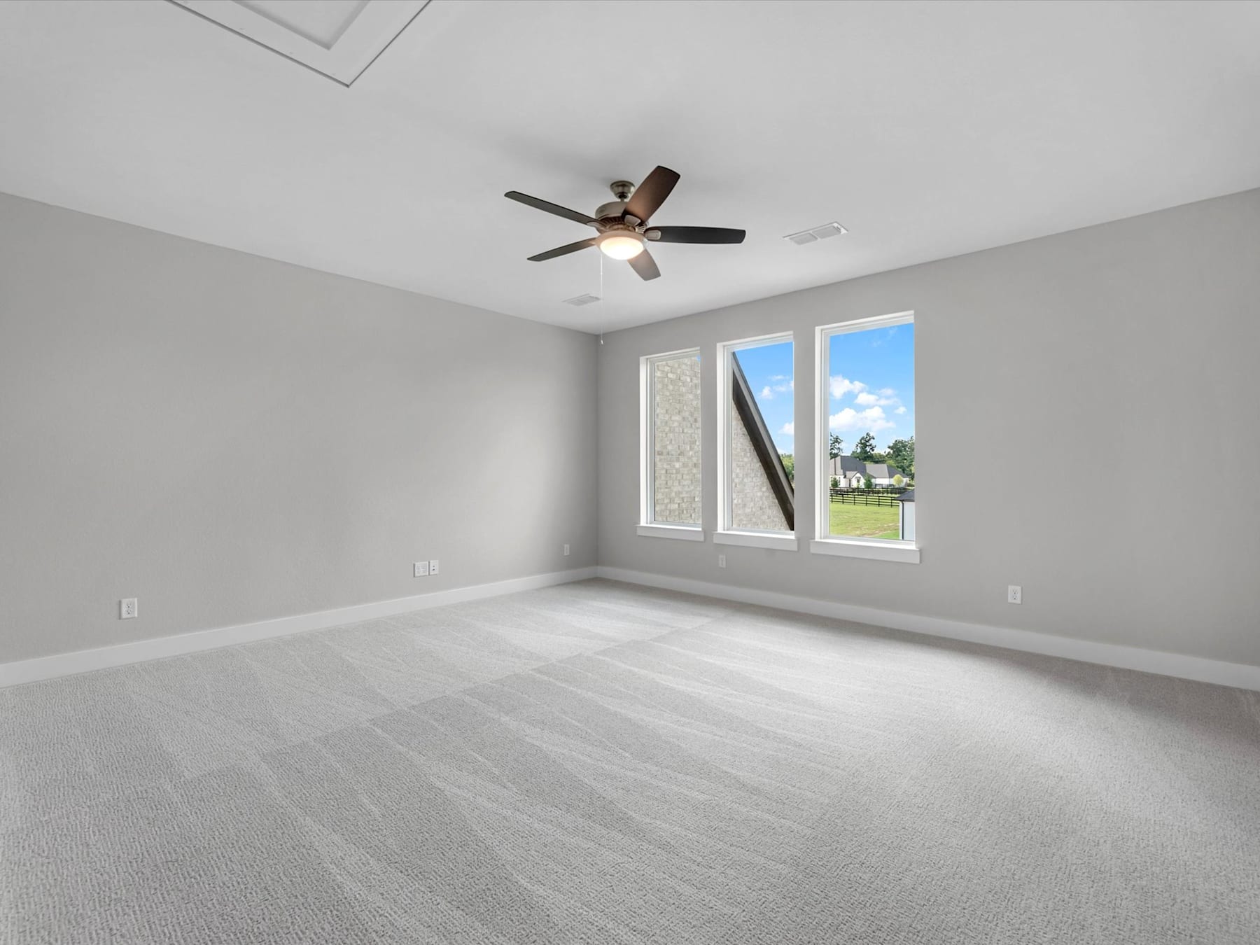 A spacious, well-lit room with a ceiling fan and large windows overlooking a grassy outdoor area.