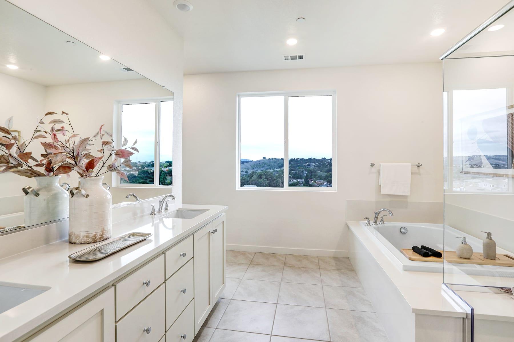 A spacious and well-lit bathroom with a large vanity, a bathtub, and a view of the cityscape through the windows.