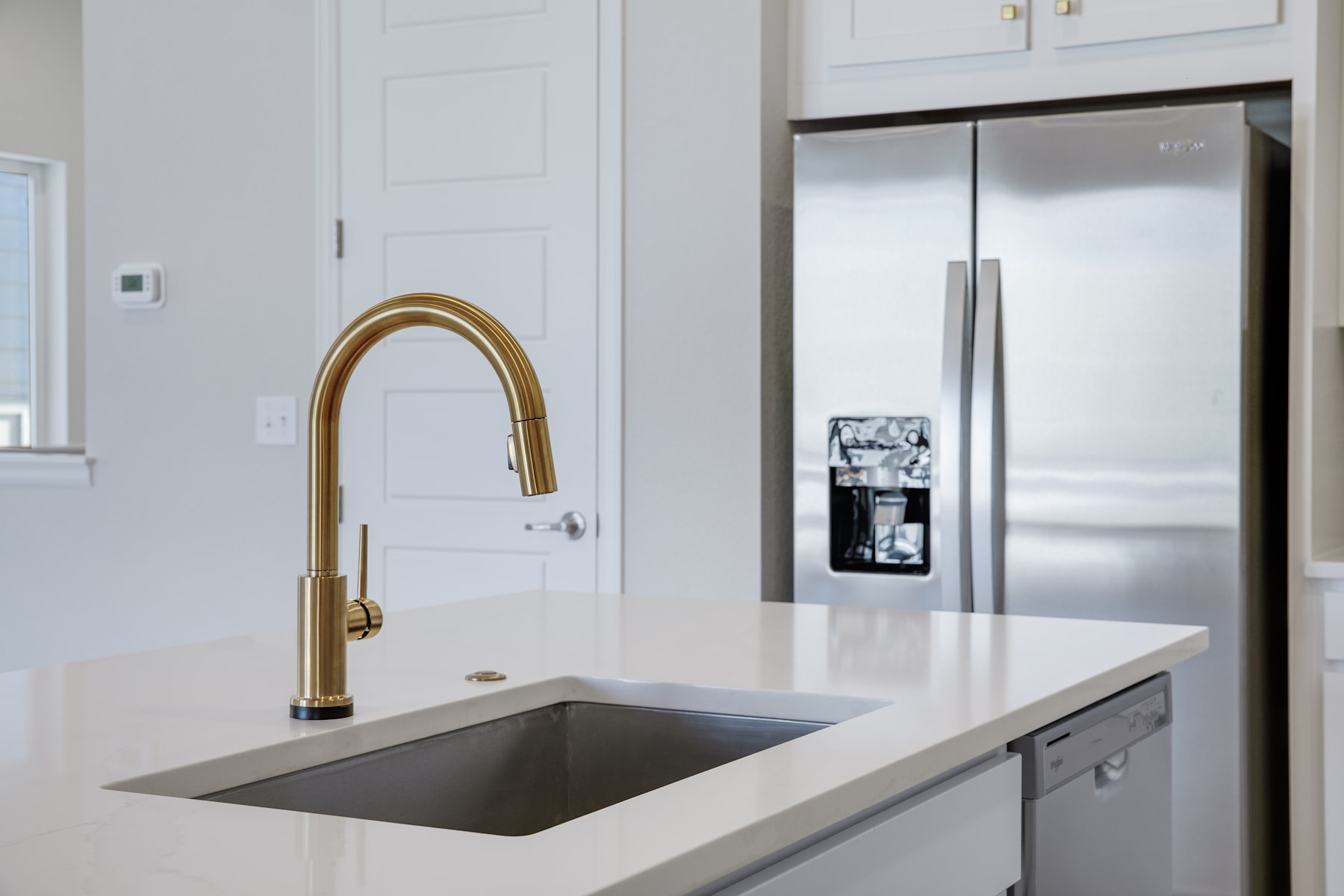 A modern kitchen with a sleek stainless steel sink, a gold-colored faucet, and a stainless steel refrigerator in the background.