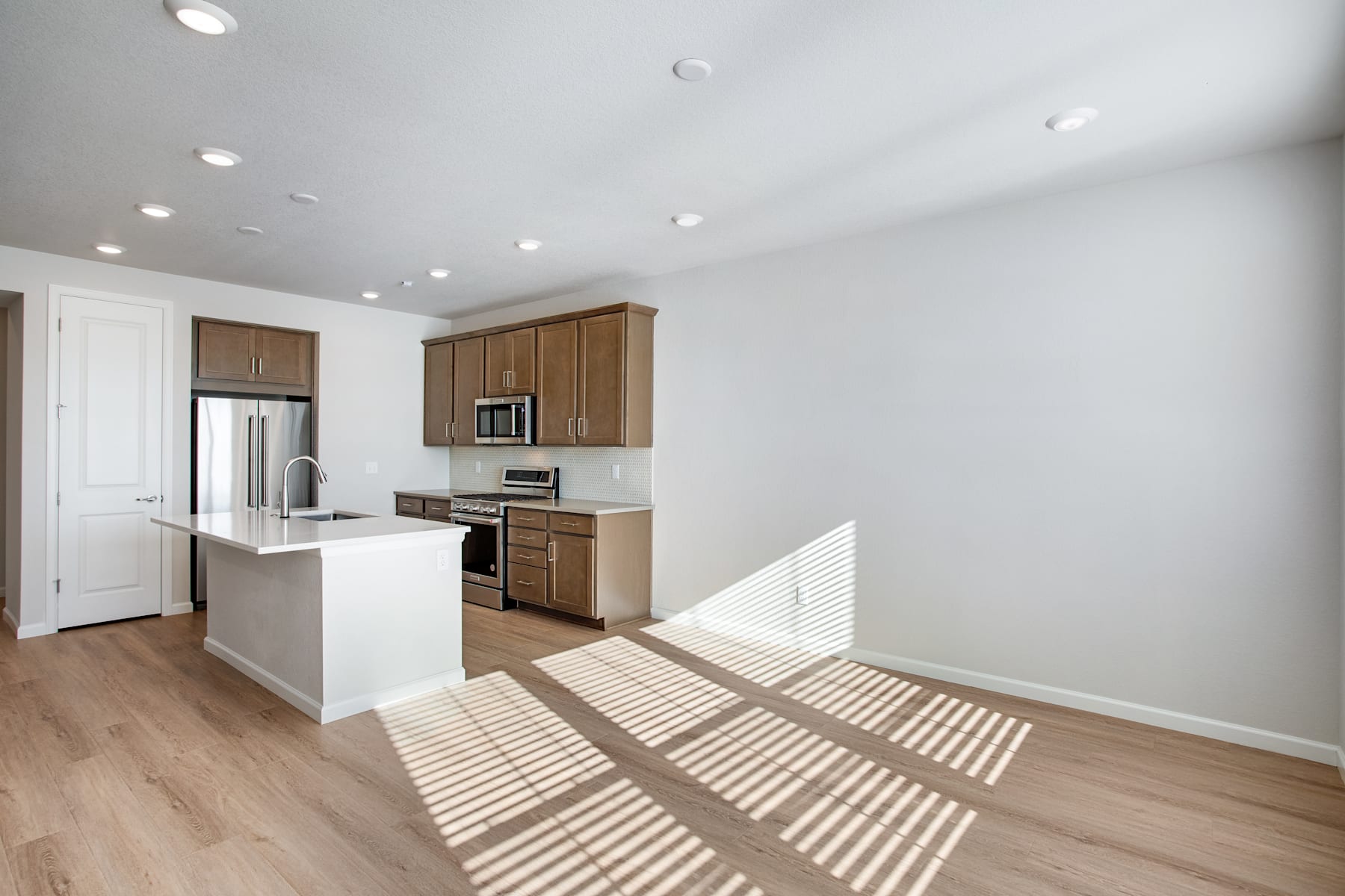 A modern, open-concept kitchen with wooden cabinets, stainless steel appliances, and a bright, airy atmosphere, with sunlight streaming in through the windows, casting warm shadows on the hardwood floor.