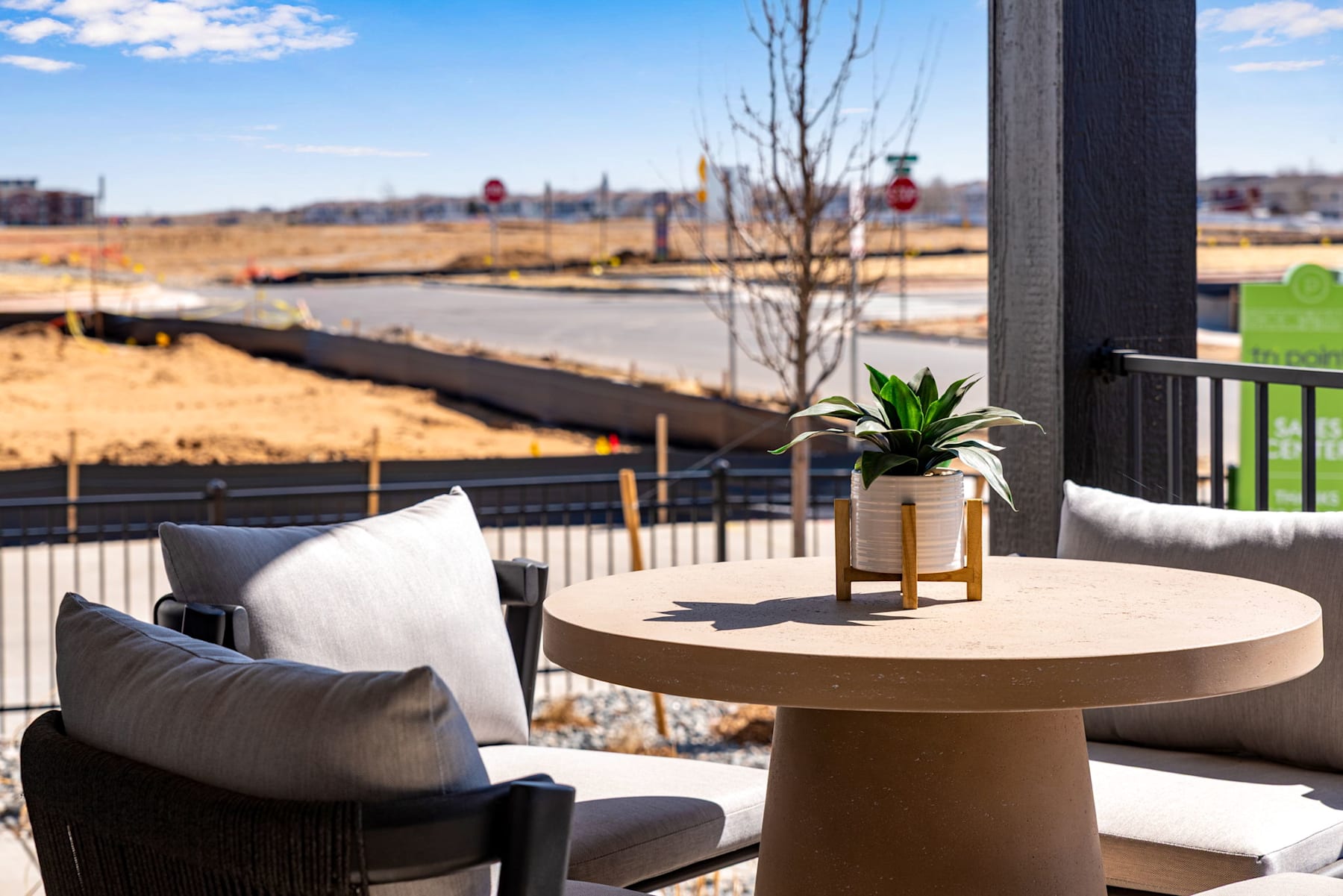 A cozy outdoor seating area with a round wooden table, a potted plant, and comfortable chairs overlooking a scenic landscape with a body of water and distant buildings.