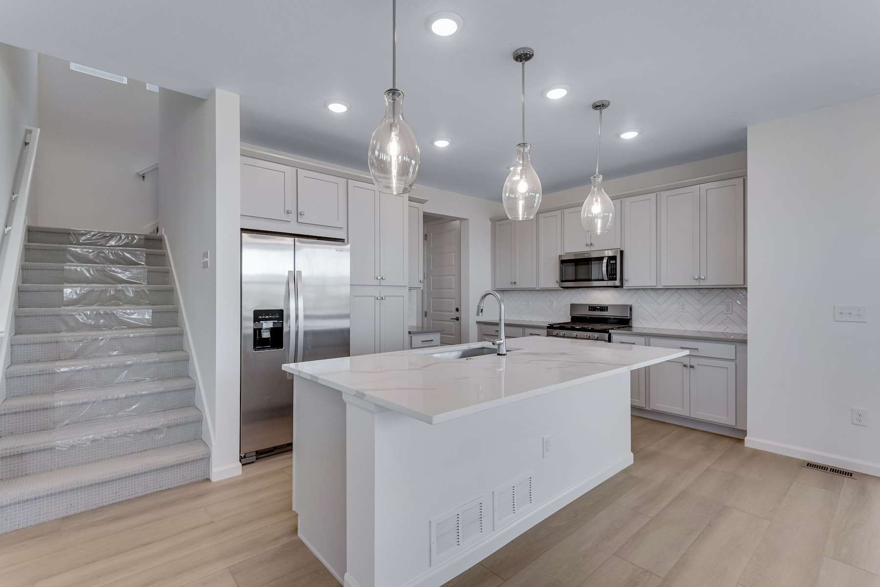 A modern, bright kitchen with white cabinets, a large island, and pendant lighting fixtures hanging from the ceiling.
