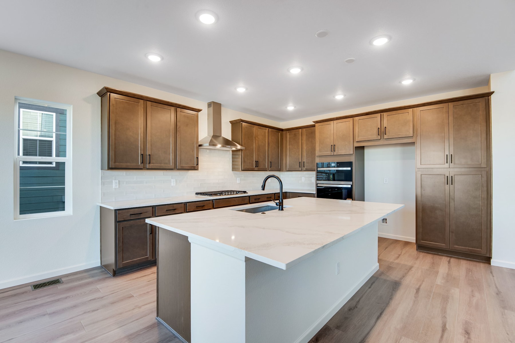 A modern, well-lit kitchen with wooden cabinets, a white countertop, and stainless steel appliances.