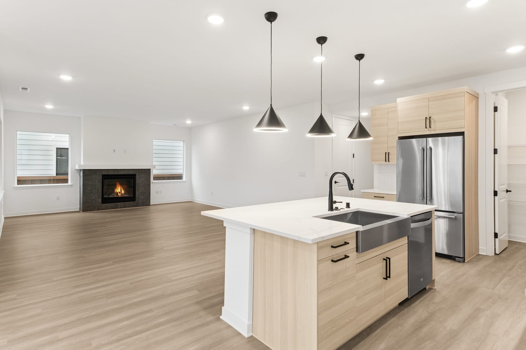 A modern, open-concept kitchen with a central island, stainless steel appliances, and pendant lighting fixtures, set against a backdrop of a cozy living area with a fireplace.
