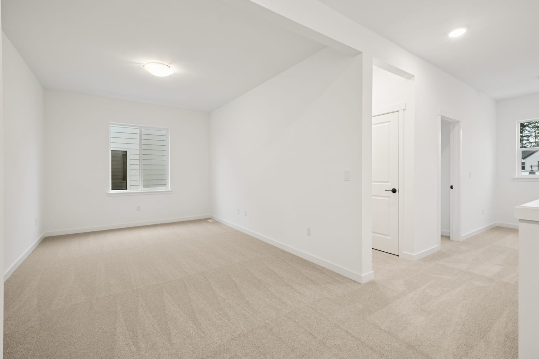 A spacious, minimalist room with white walls, a wooden floor, and a window providing natural light.