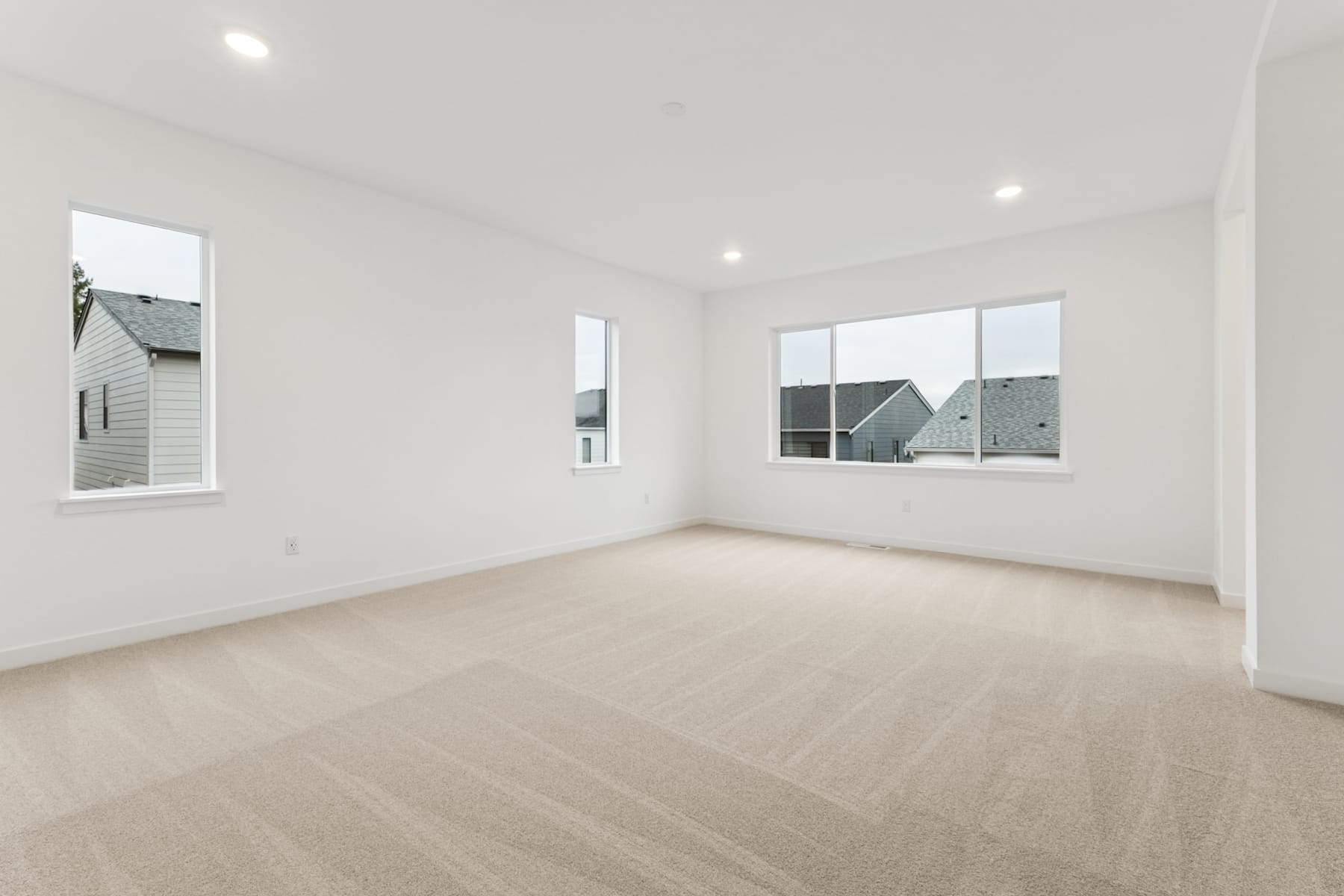 A spacious, well-lit room with white walls, hardwood floors, and large windows providing a view of the exterior.