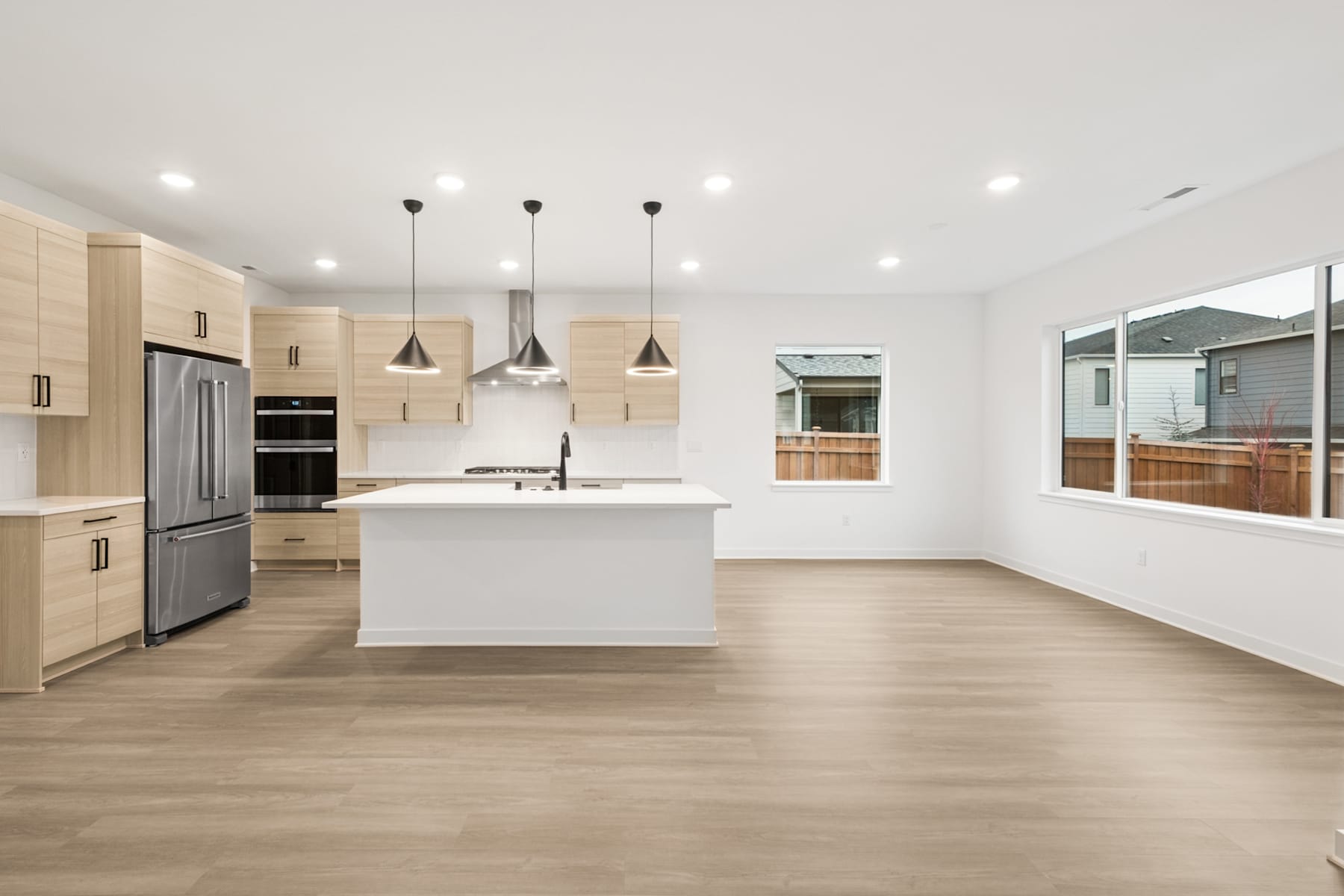 A modern, open-concept kitchen with light-colored cabinets, a central island, and pendant lighting fixtures hanging from the ceiling.