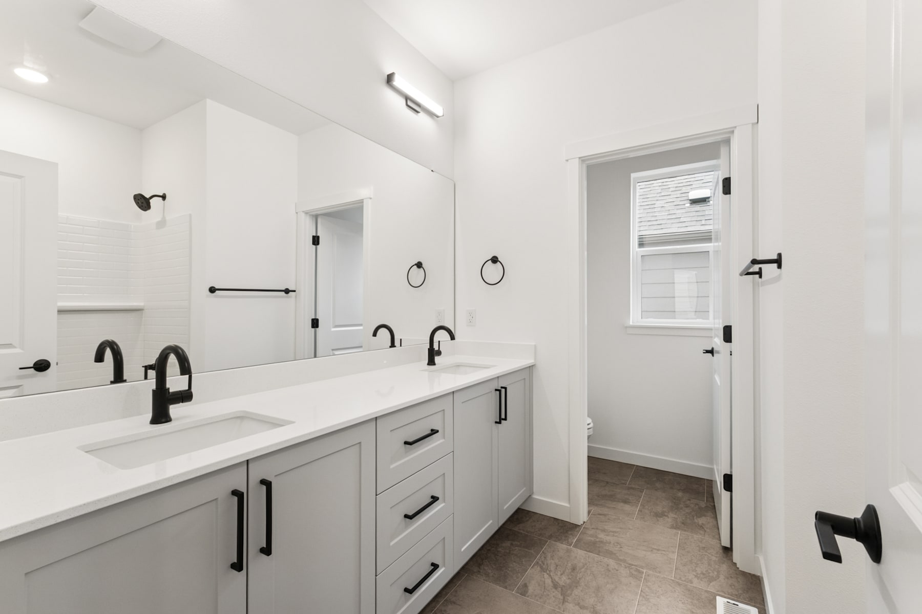 A modern, minimalist bathroom with a double vanity, black fixtures, and a doorway leading to another room.