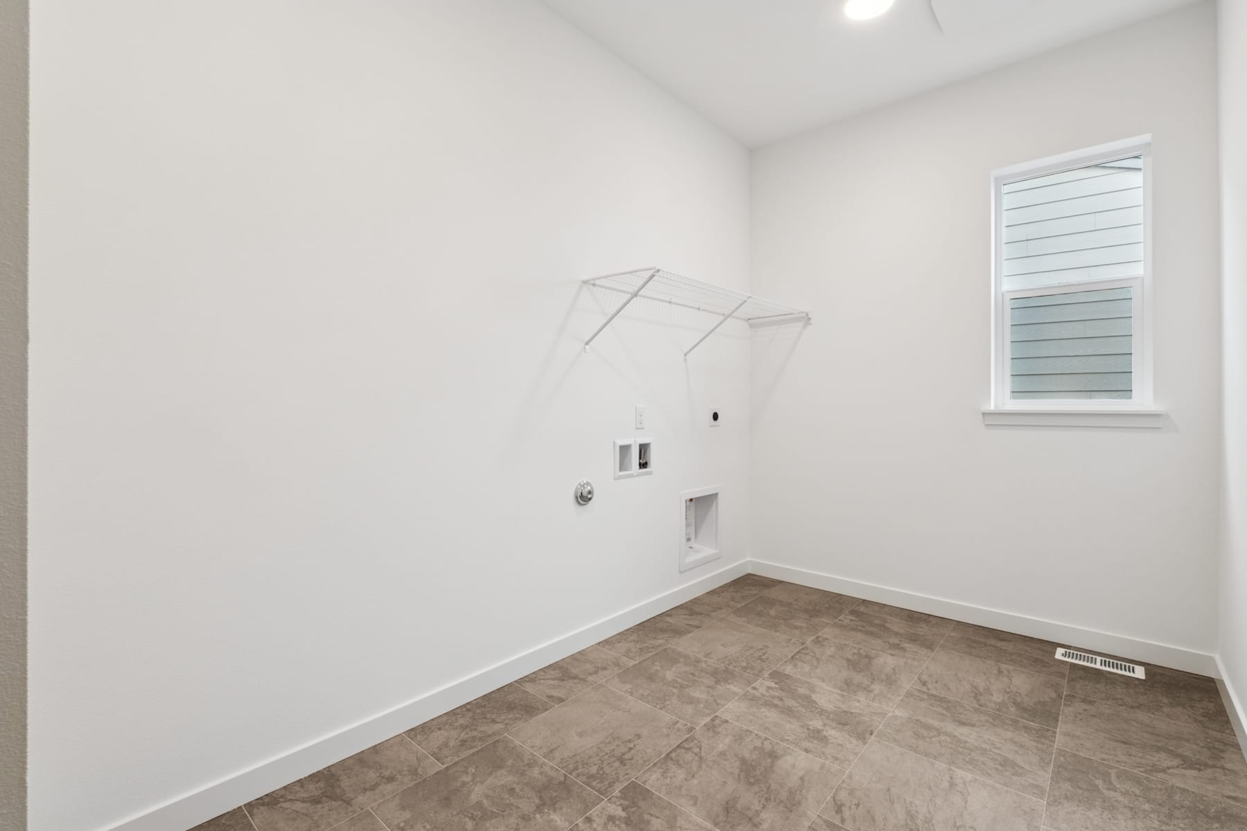 A small, empty room with white walls and a tiled floor, featuring a clothes drying rack mounted on the wall.