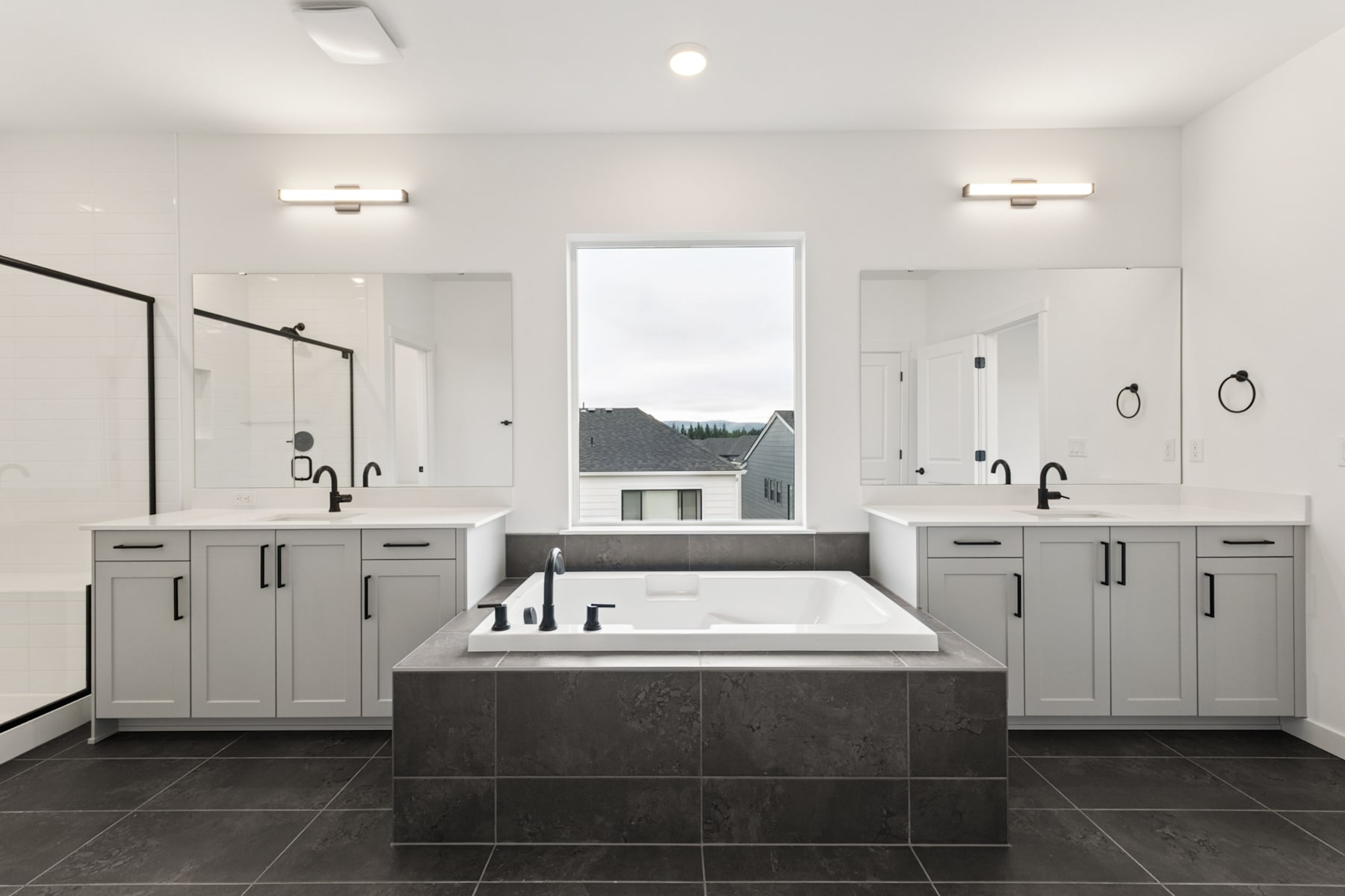 A spacious and modern bathroom with a large bathtub, double vanity, and a window overlooking the exterior landscape.