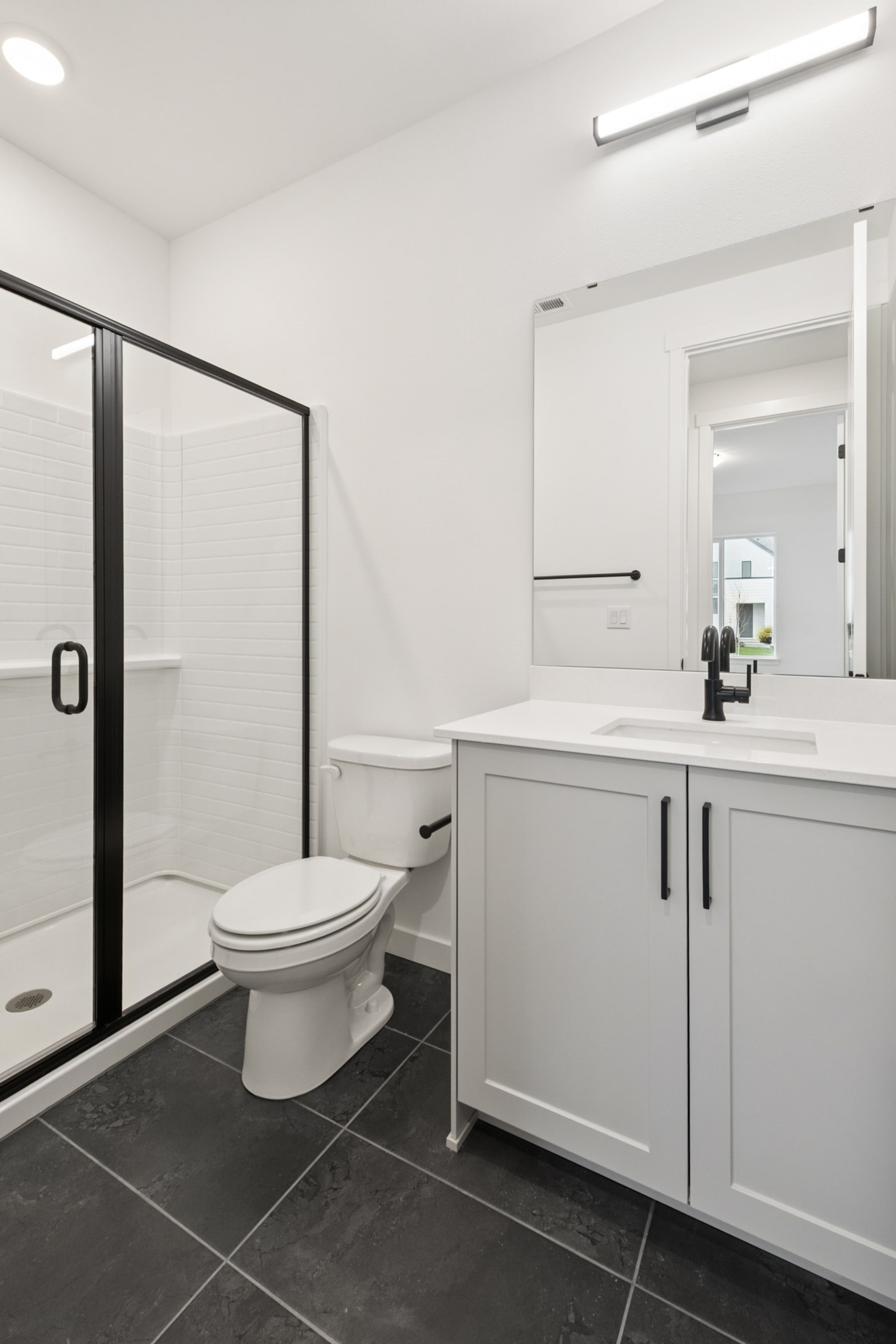 A modern, minimalist bathroom with white cabinets, a toilet, and a large mirror on the wall.