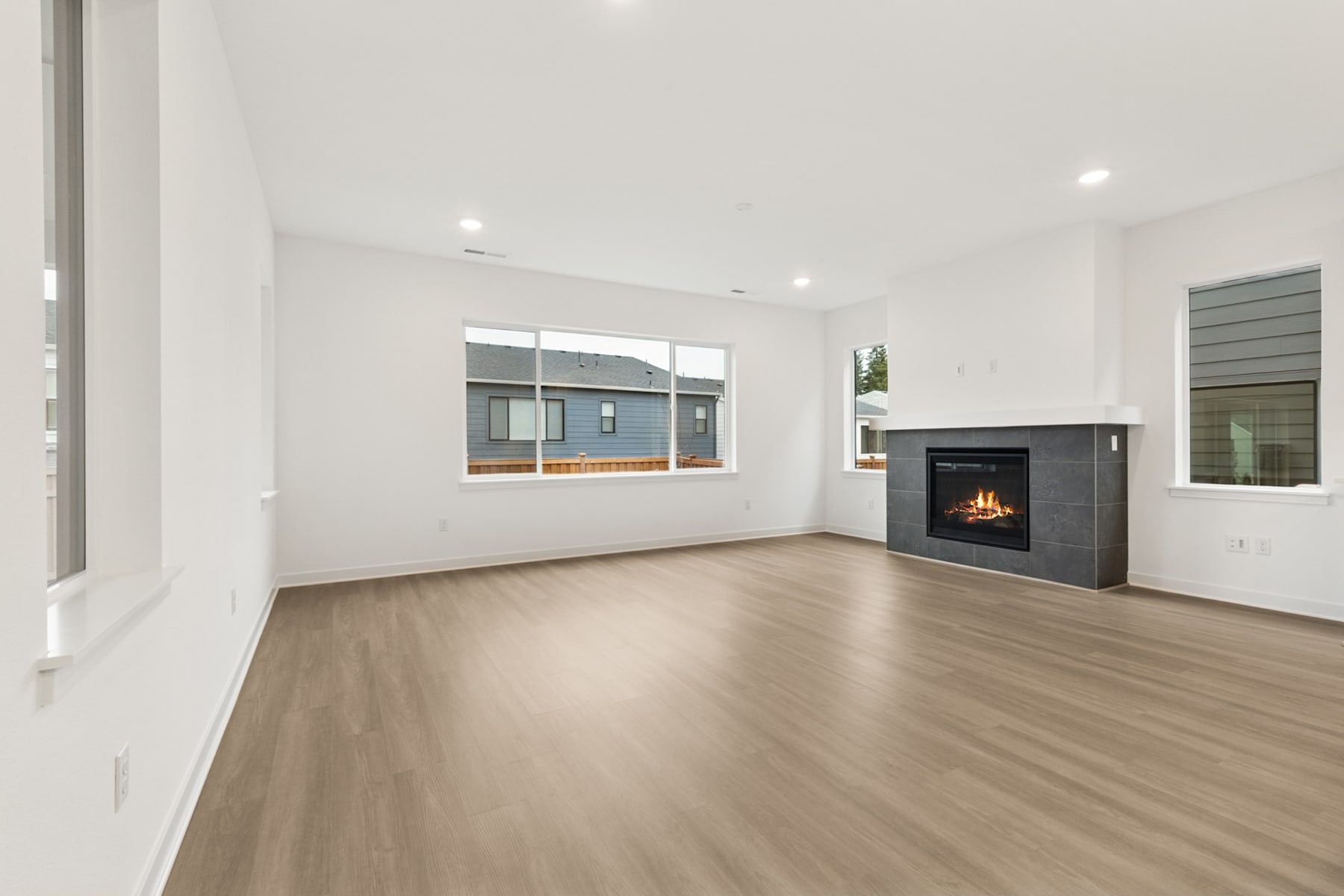 A spacious, modern living room with a fireplace and large windows, featuring a hardwood floor and a minimalist, neutral-toned decor.