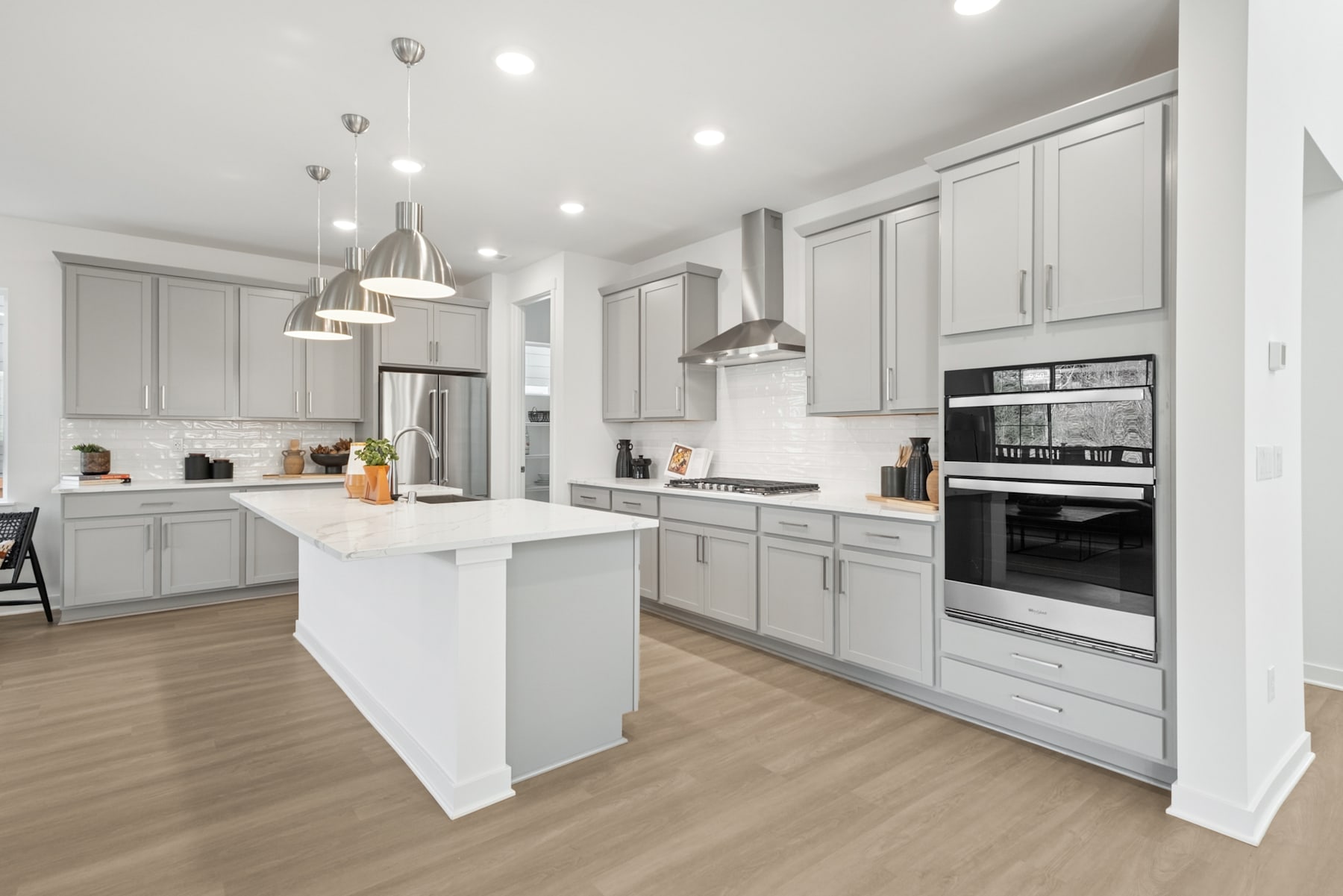 A modern, open-concept kitchen with white cabinets, a central island, and pendant lighting fixtures, set against a hardwood floor.