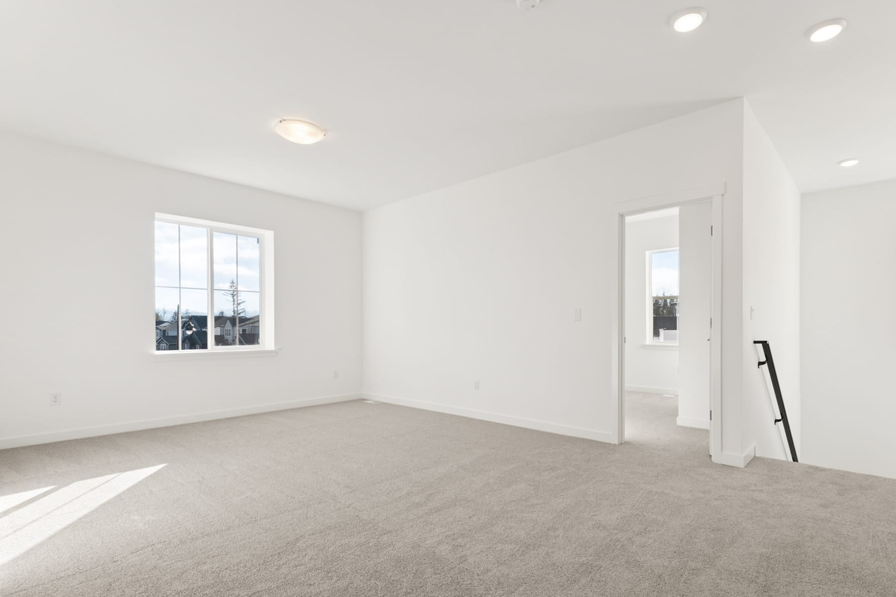 An empty, bright room with white walls, a carpeted floor, and recessed lighting fixtures.