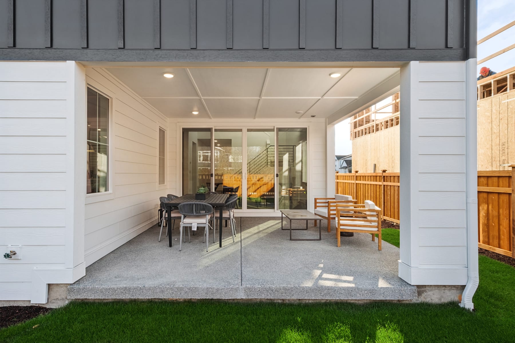 A modern, open-concept patio with a dining area, comfortable seating, and a grassy backyard visible through the glass doors.
