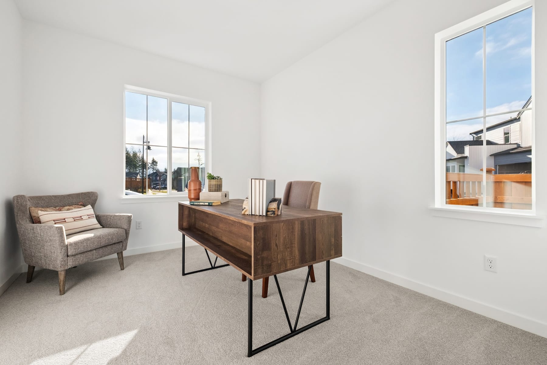 A cozy and minimalist living room with a comfortable armchair, a wooden console table, and large windows providing natural light and a view of the outdoors.