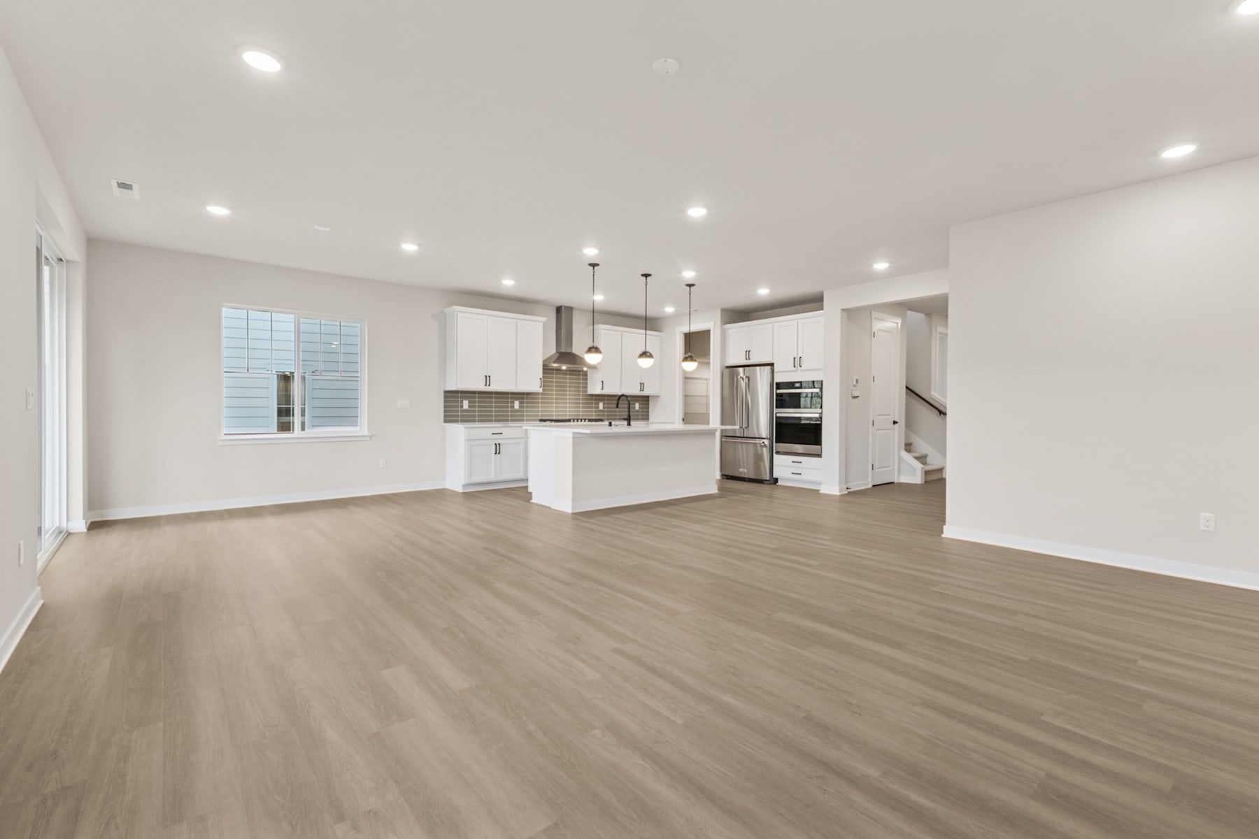 A spacious, open-concept kitchen and living room with white cabinets, stainless steel appliances, and hardwood flooring.