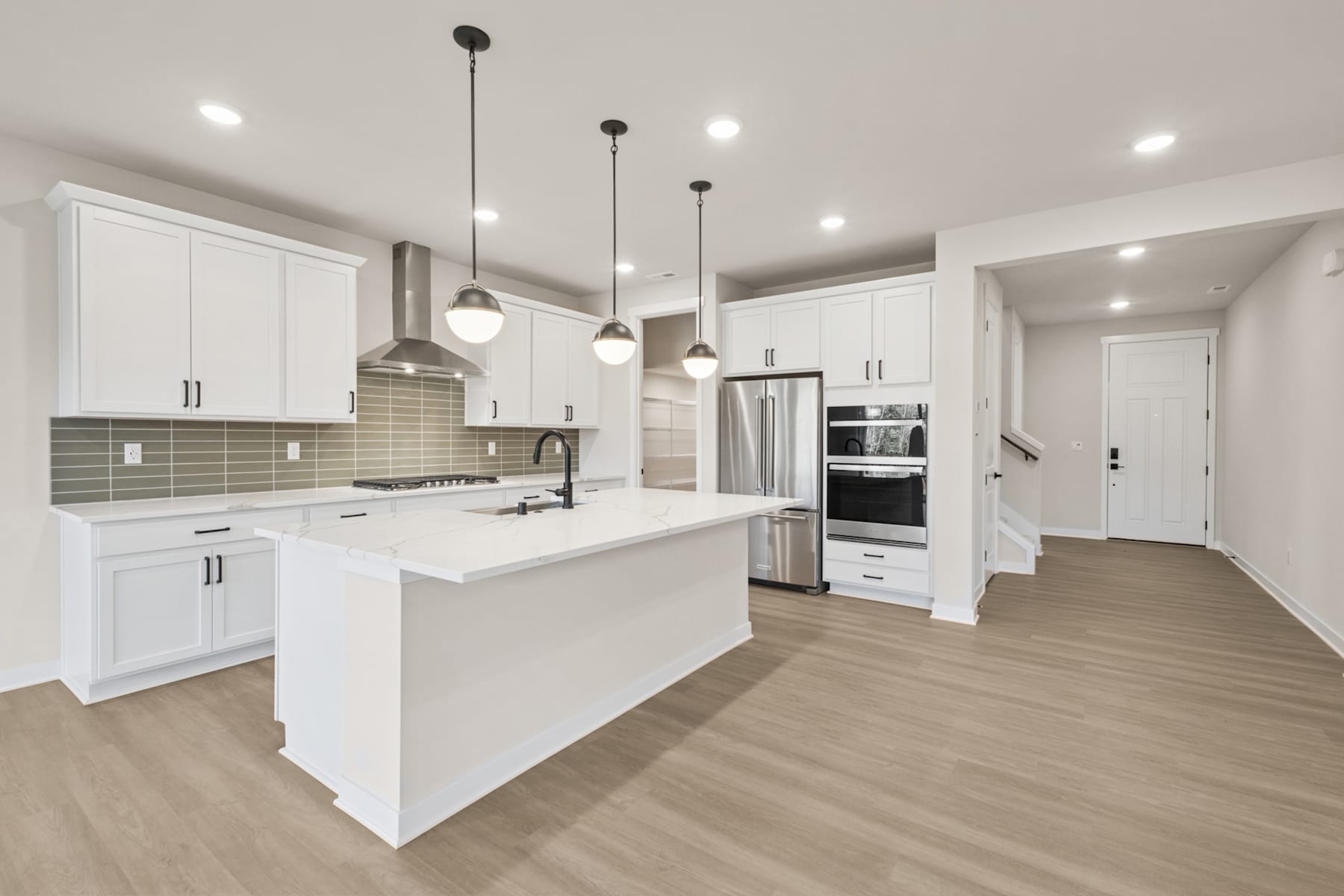 A modern, open-concept kitchen with white cabinets, a large island, and pendant lighting fixtures, set against a light-colored hardwood floor.
