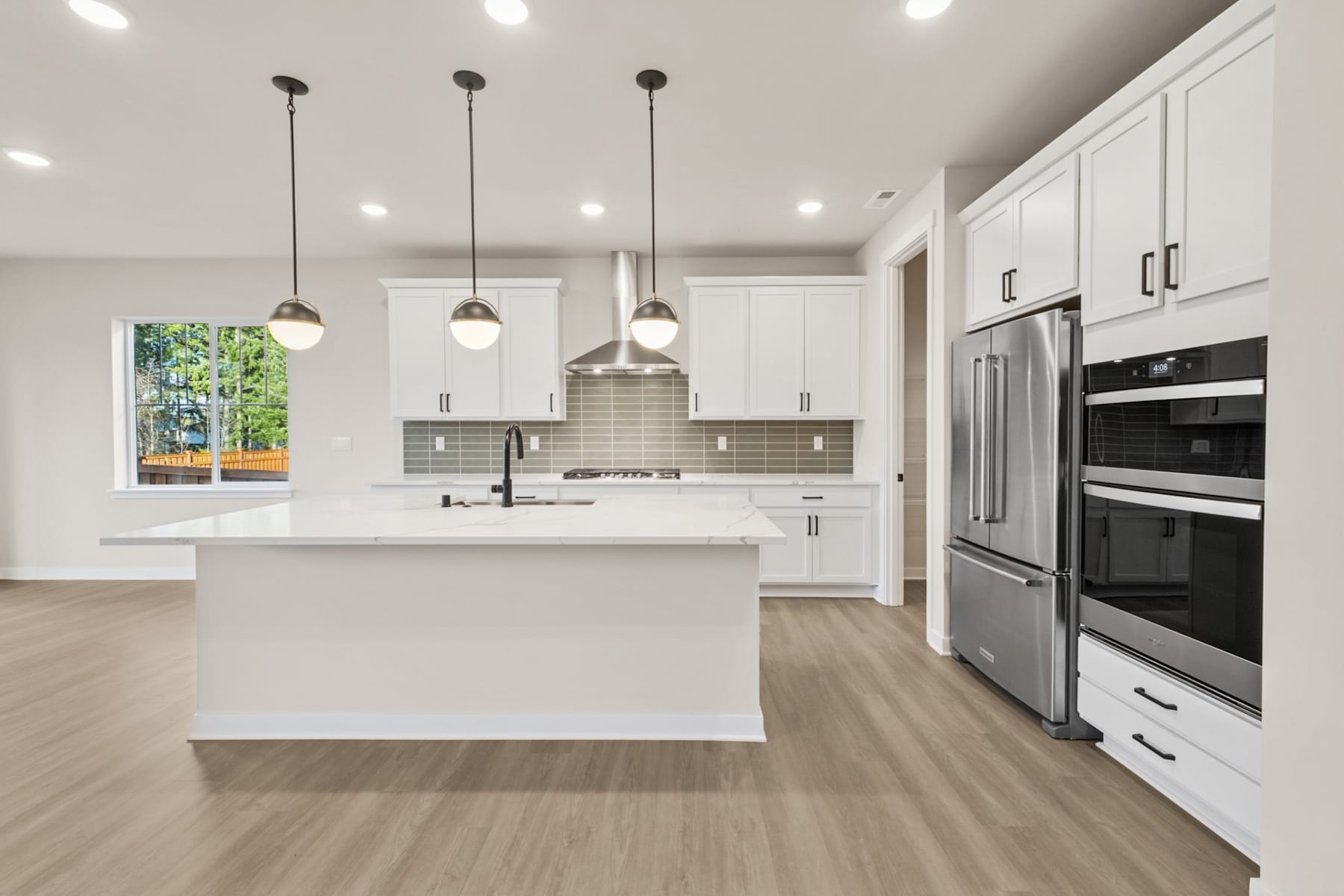 A modern, bright kitchen with white cabinets, stainless steel appliances, and a central island with pendant lighting.