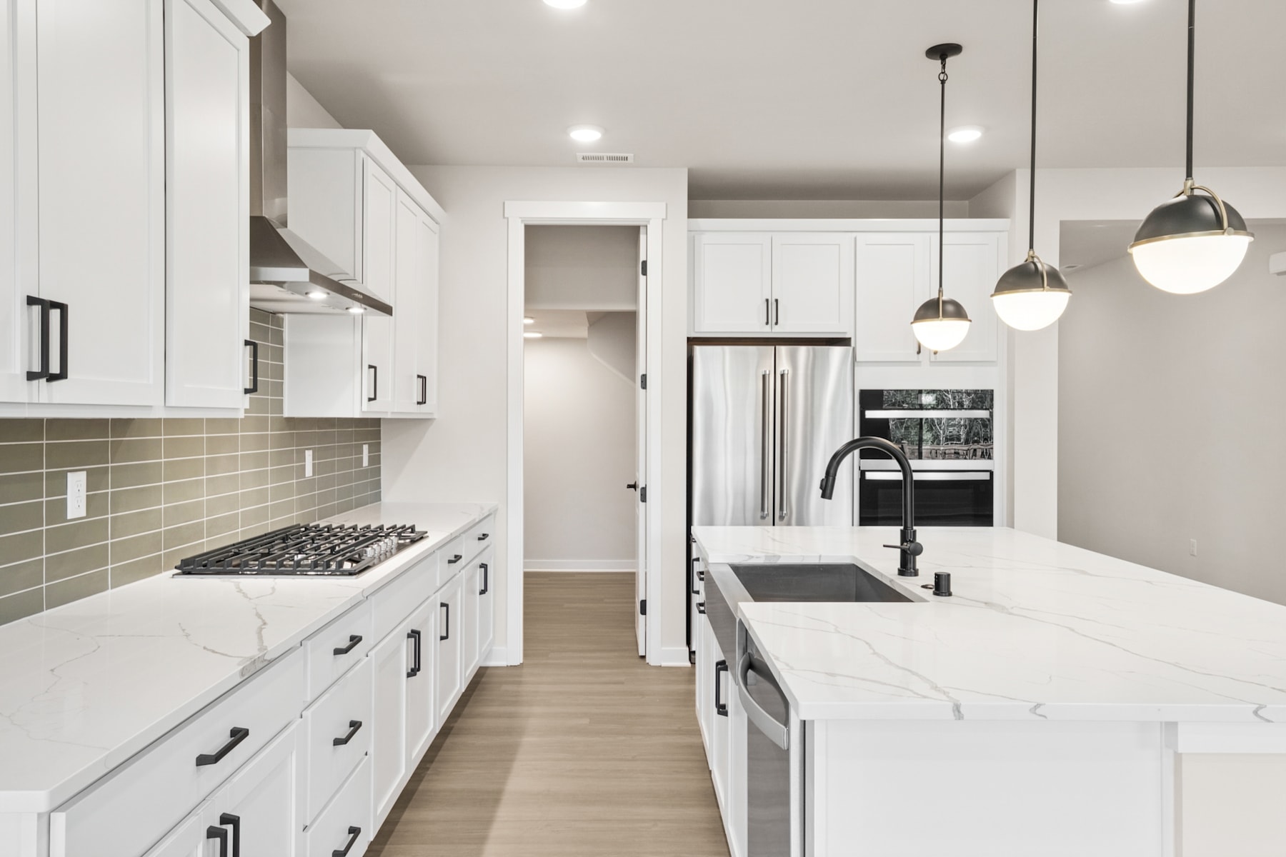 A modern, minimalist kitchen with white cabinets, a marble countertop, and pendant lighting fixtures, creating a bright and airy atmosphere.