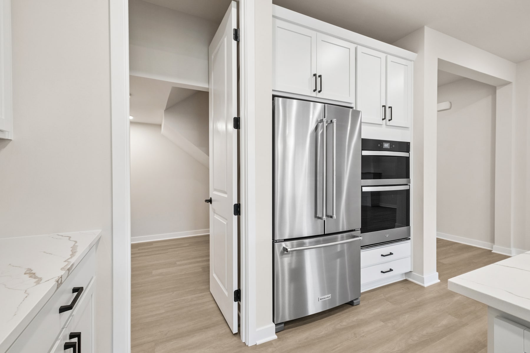 A modern, minimalist kitchen with white cabinets, stainless steel appliances, and a hardwood floor.
