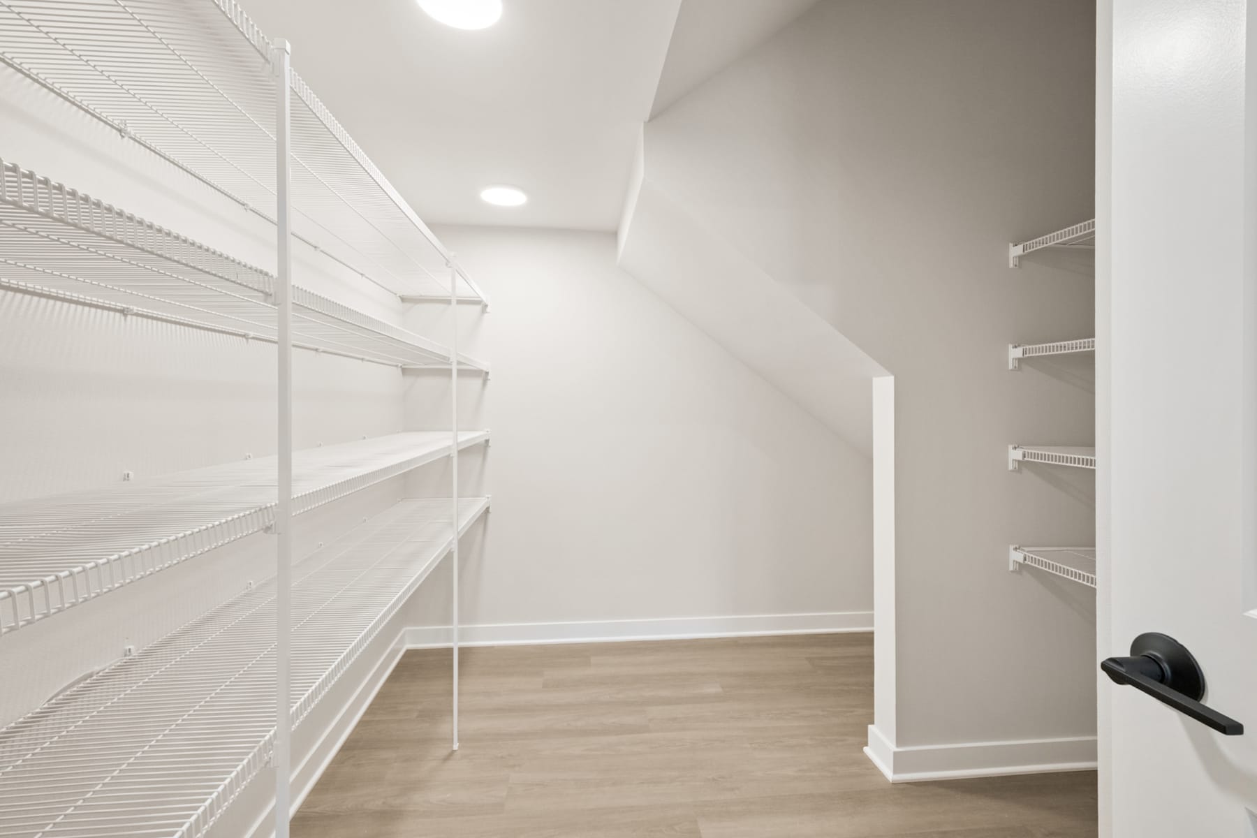 A spacious, well-lit walk-in closet with white shelves and a wooden floor.