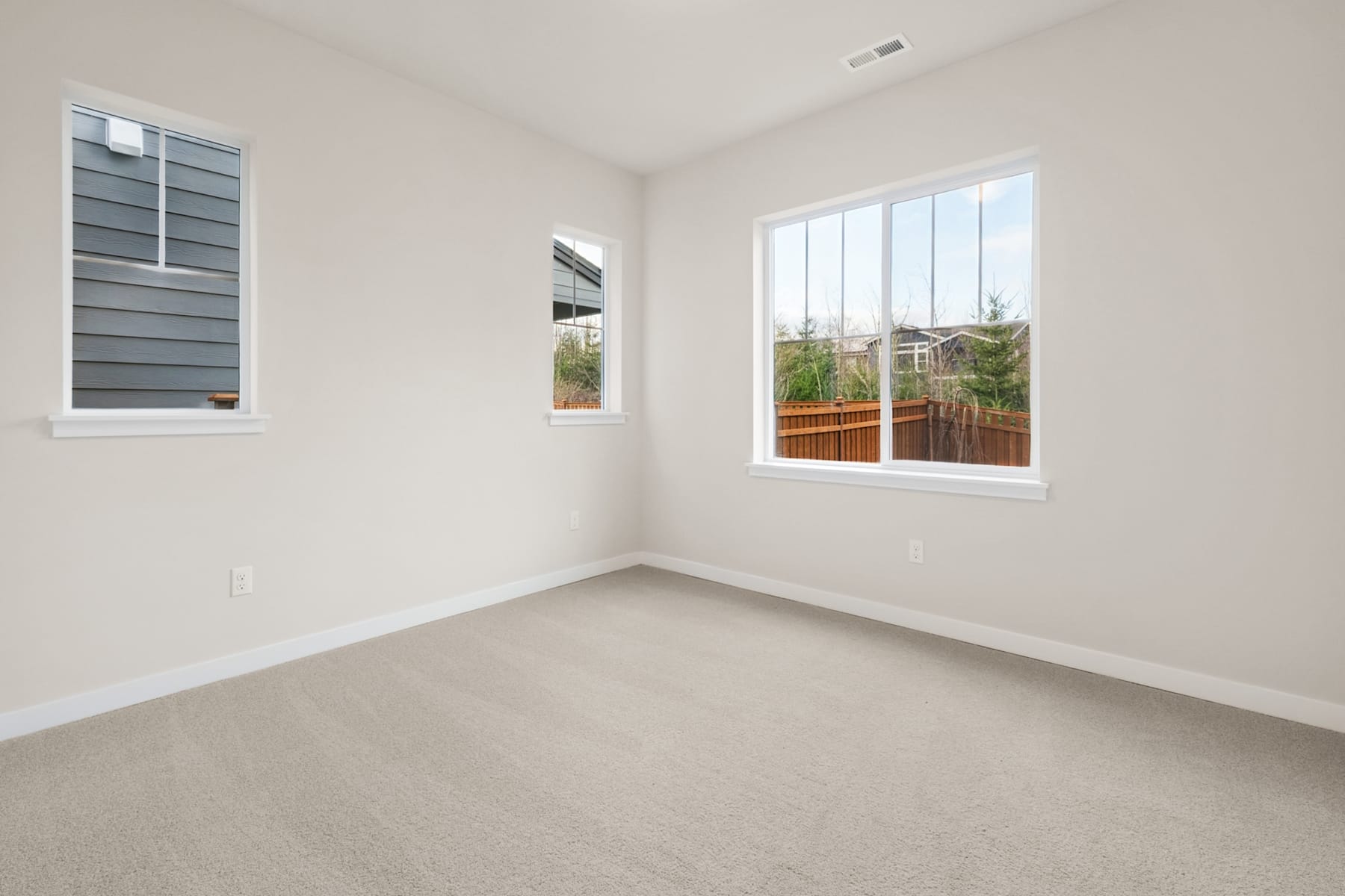 A bright, empty room with large windows overlooking a backyard area.