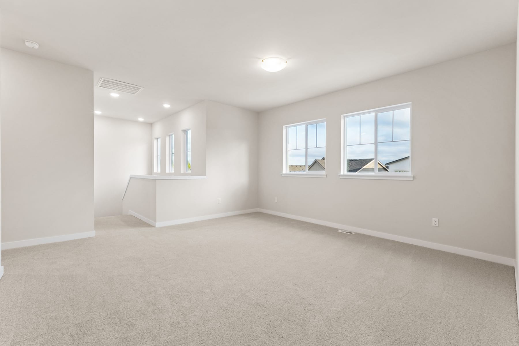 An empty, bright, and spacious room with white walls, carpeted floor, and large windows allowing natural light to fill the space.
