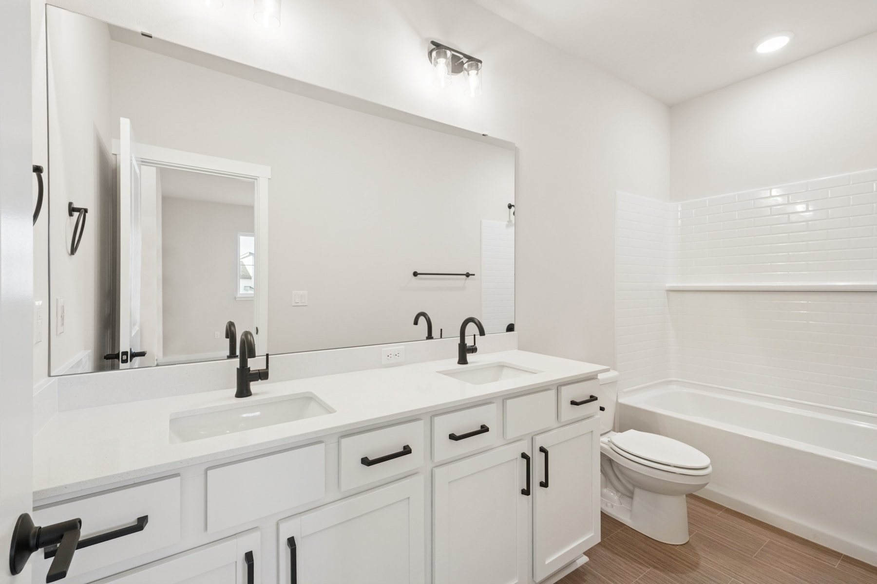 A modern, minimalist bathroom with a double vanity, white cabinets, and black hardware, set against a bright, airy backdrop.
