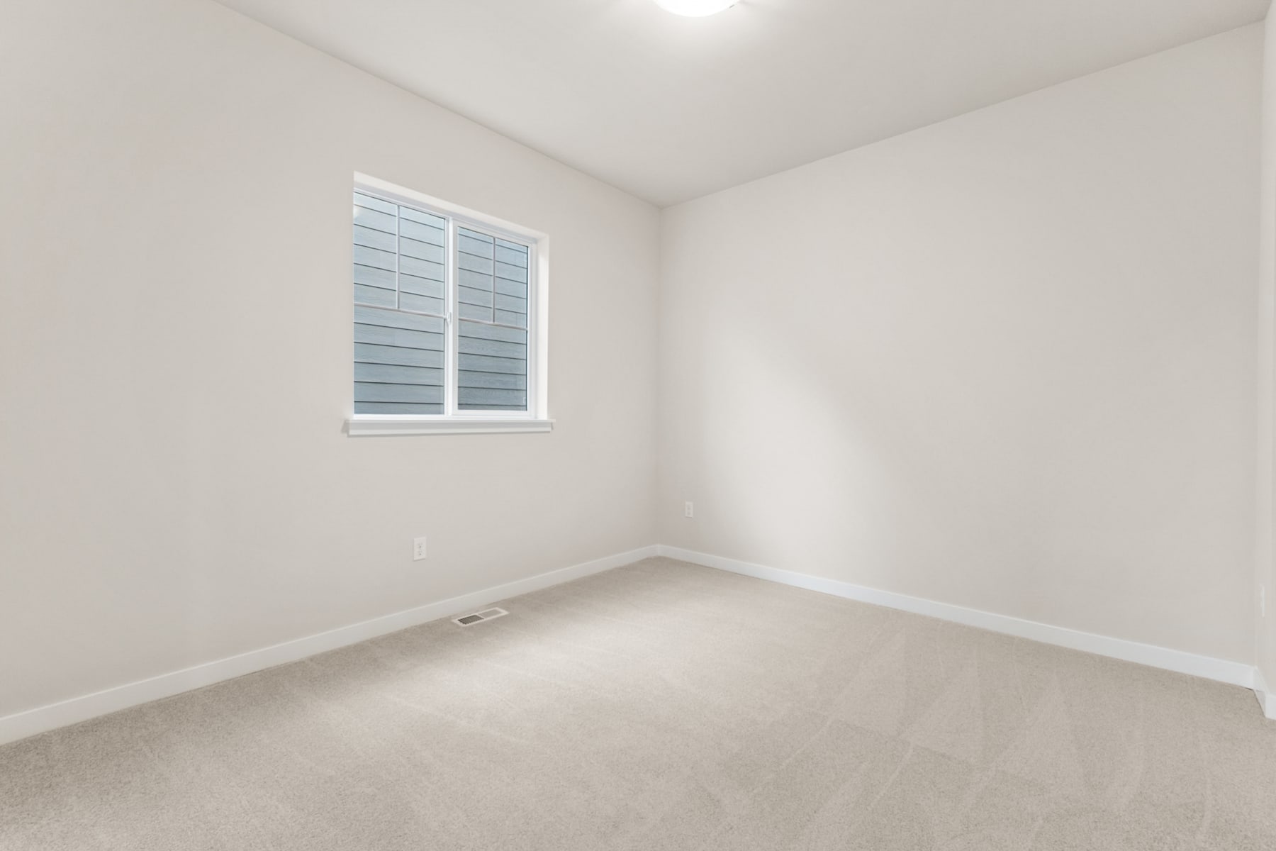 A bright, empty room with a window and white walls, featuring a clean and minimalist interior design.