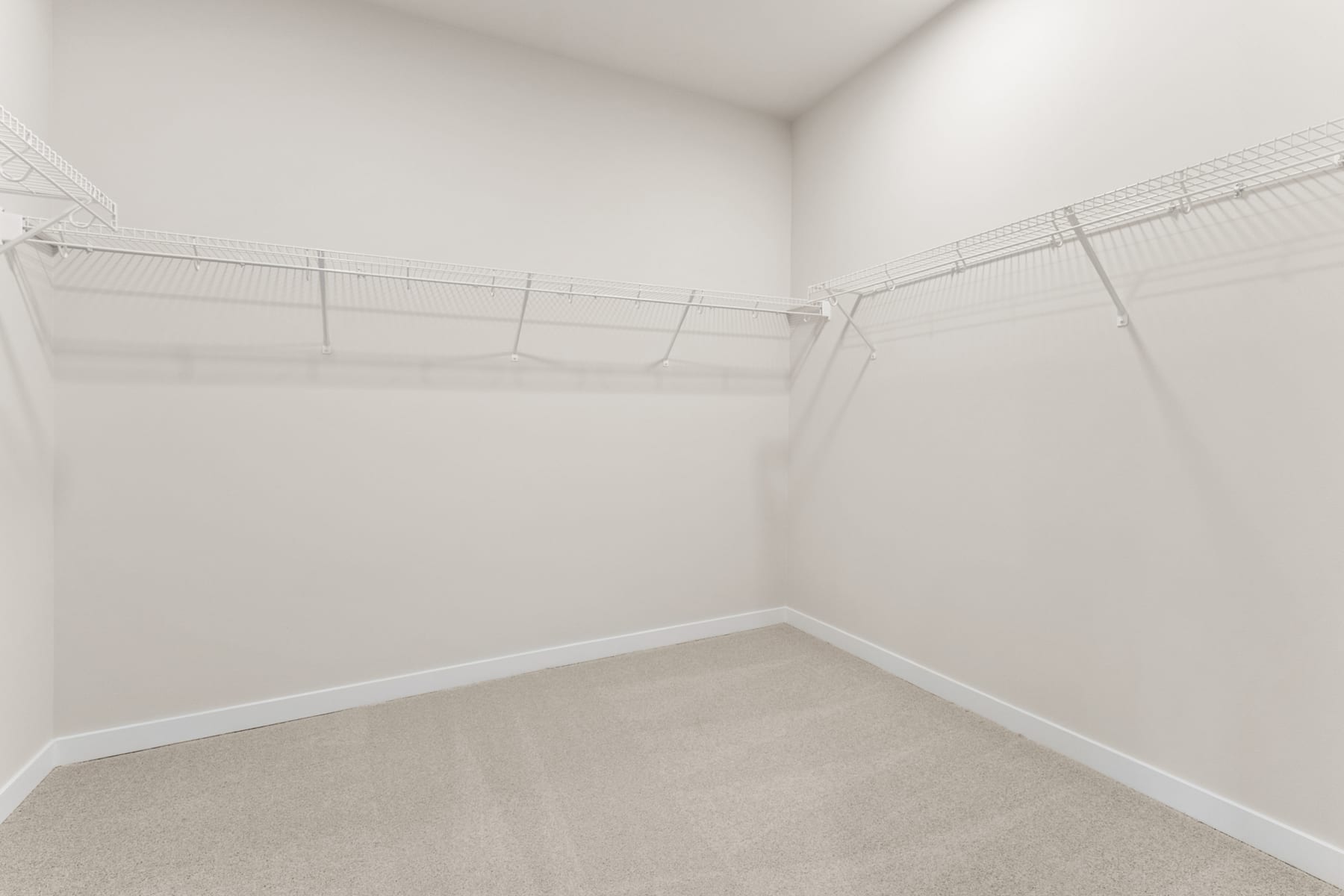 A spacious, well-lit closet with white walls, a carpeted floor, and a wire shelving system installed along the walls.