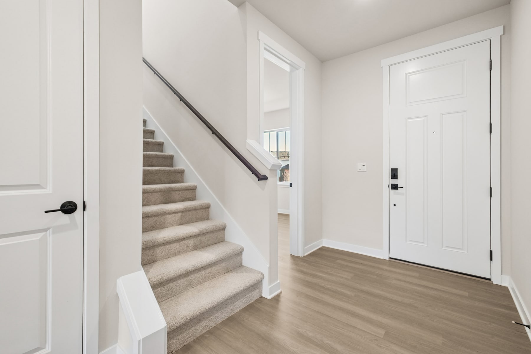 A bright and spacious entryway with a staircase leading up, hardwood floors, and a white door in the background.