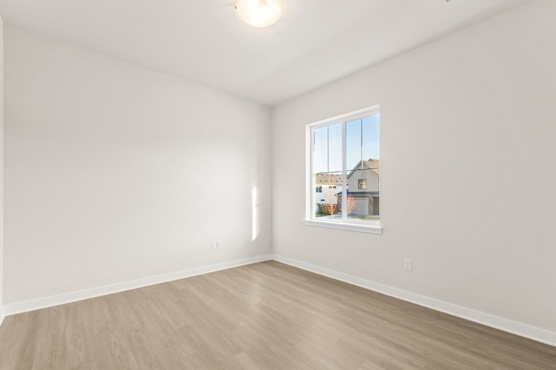 A bright, empty room with a single window and a hardwood floor.