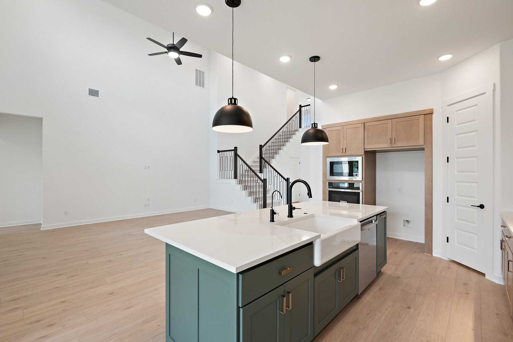 A modern, open-concept kitchen with a large island, pendant lighting, and a staircase visible in the background.