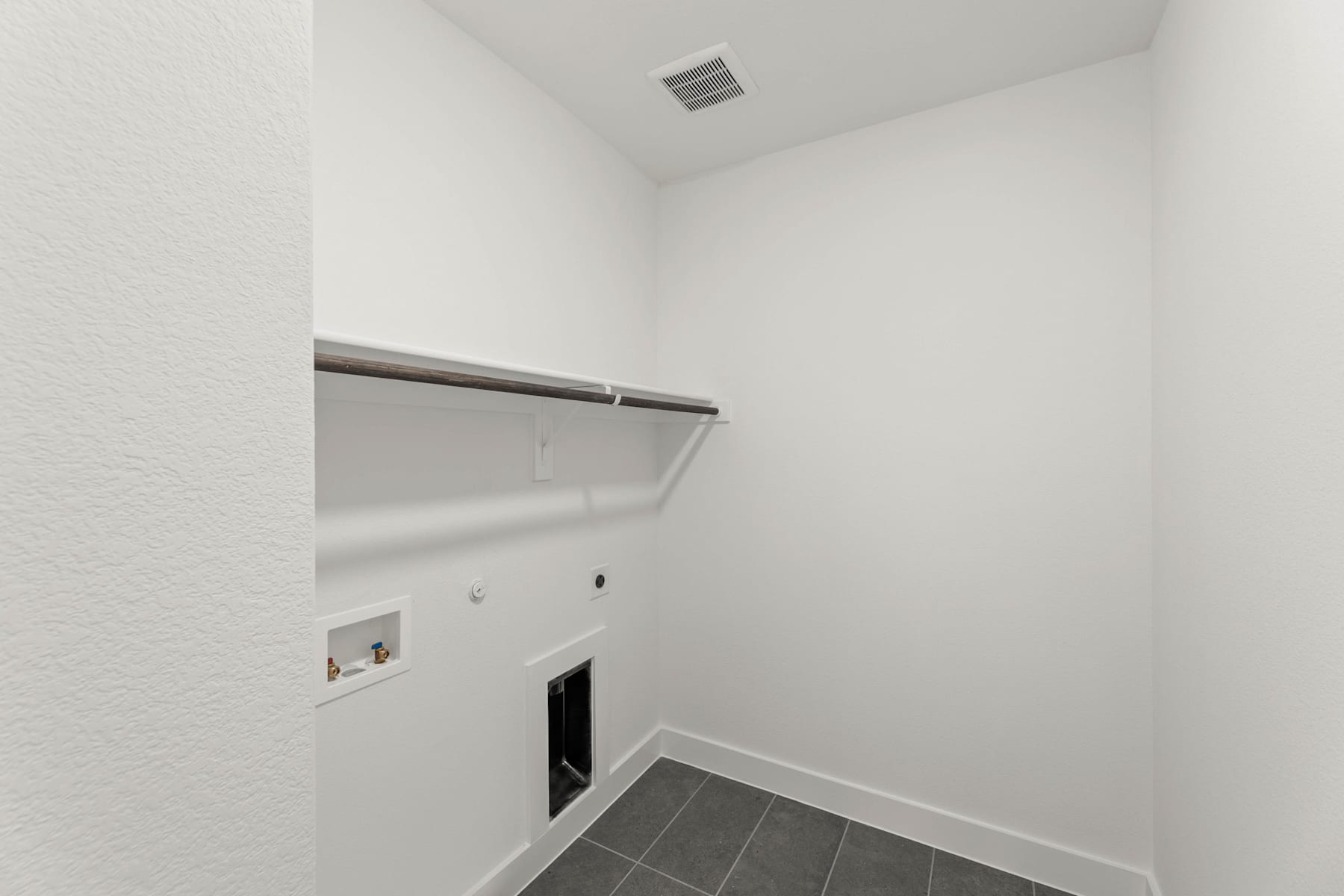 A white-walled room with a gray tiled floor and a metal clothing rod mounted on the wall, suggesting a closet or storage space.